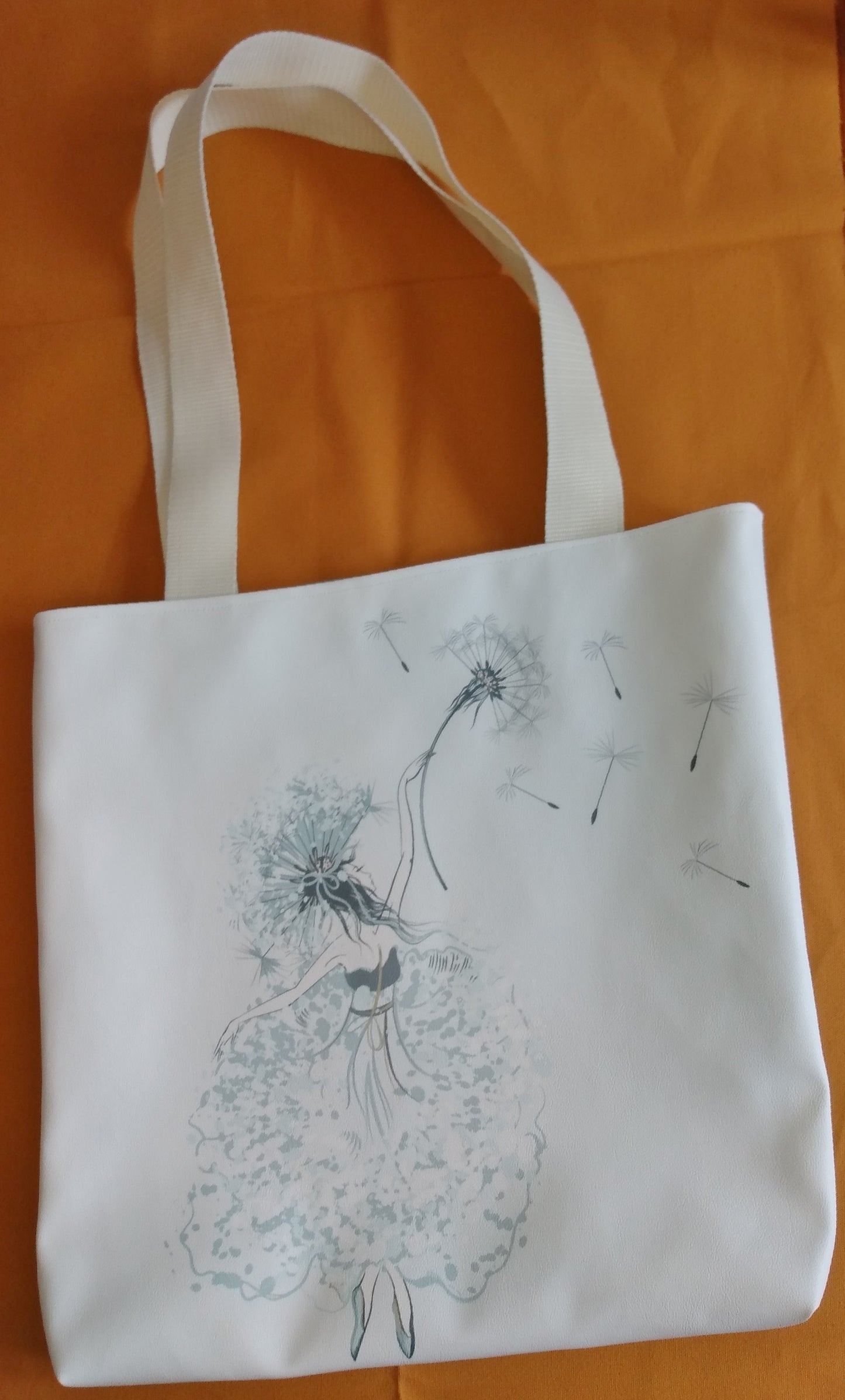 Face avant du sac Tara. Elle est en simili cuir blanc cassé, au centre est dessinée une danseuse tenant un pissenlit dans sa main. Les anses sont aussi couleur blanc cassé.