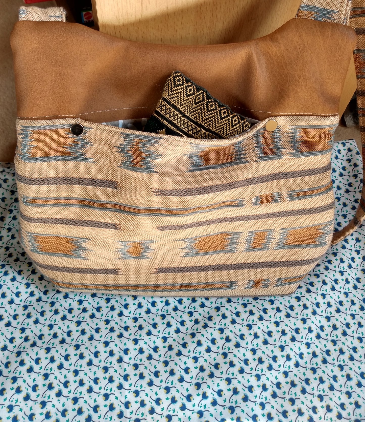 arrière du sac pivoine marron. Le bas du sac est en tissu type jacquard beige avec des touches bleutées et marrons. Le haut du sac est en simili cuir marron. Une poche ouverte est disponible à l'arrière du sac. ici, un objet est à l'intérieur.