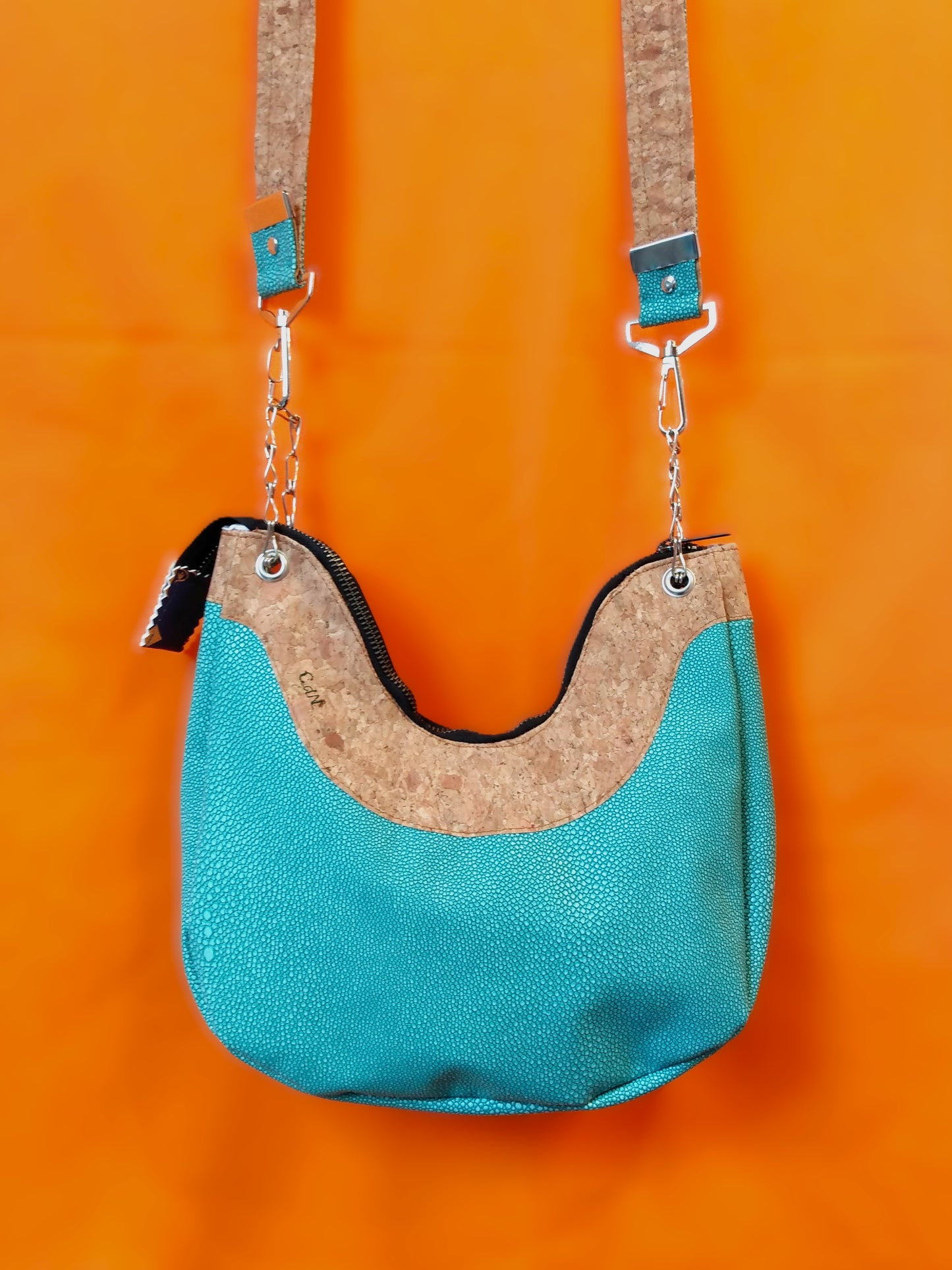 Arrière du sac Melbourne. Haut du sac en liège marron clair, sur une bande de environ 8 cm de large. Le reste du sac est en simili cuir émeraude à grains. La bandoulière est accrochée via chainettes et mousquetons en métal. Elle est bicolore émeraude à grain et liège. Une fermeture noire permet de fermer le sac.