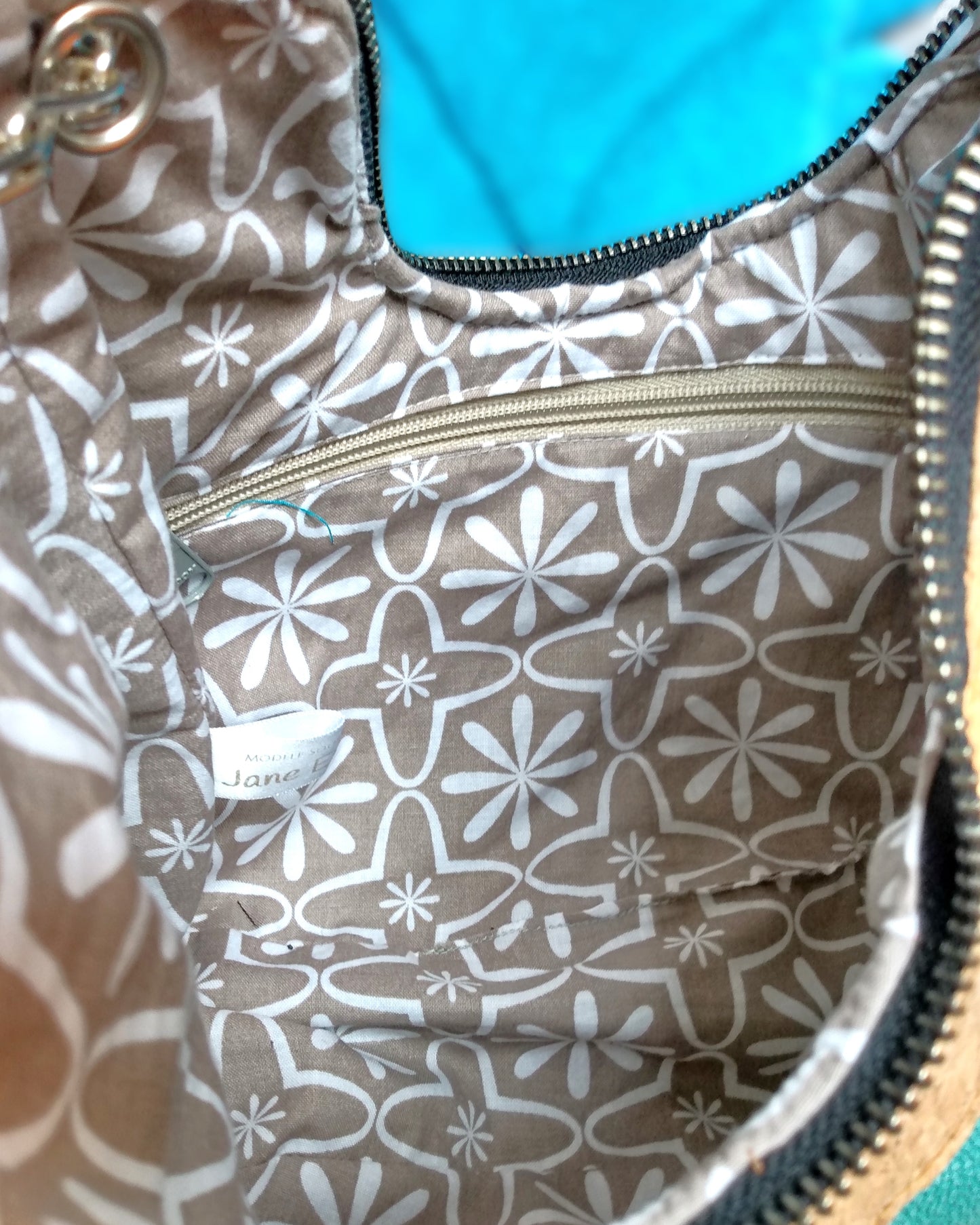 Intérieur du sac Melbourne. Doublure couleur taupe avec des motifs fleurs chaya blanches. Une poche zippée à fermeture éclair beige.