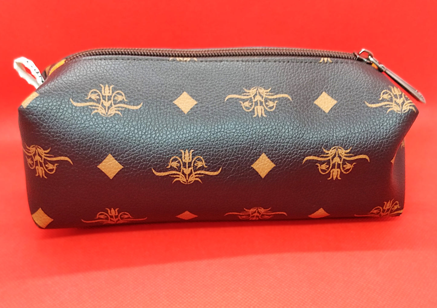 Trousse taille 1 simili cuir marron foncé à fleurs et losanges orangés. Se ferme par une fermeture éclair marron. L'étiquette "CdN" de la marque est présente sur un côté de la trousse.