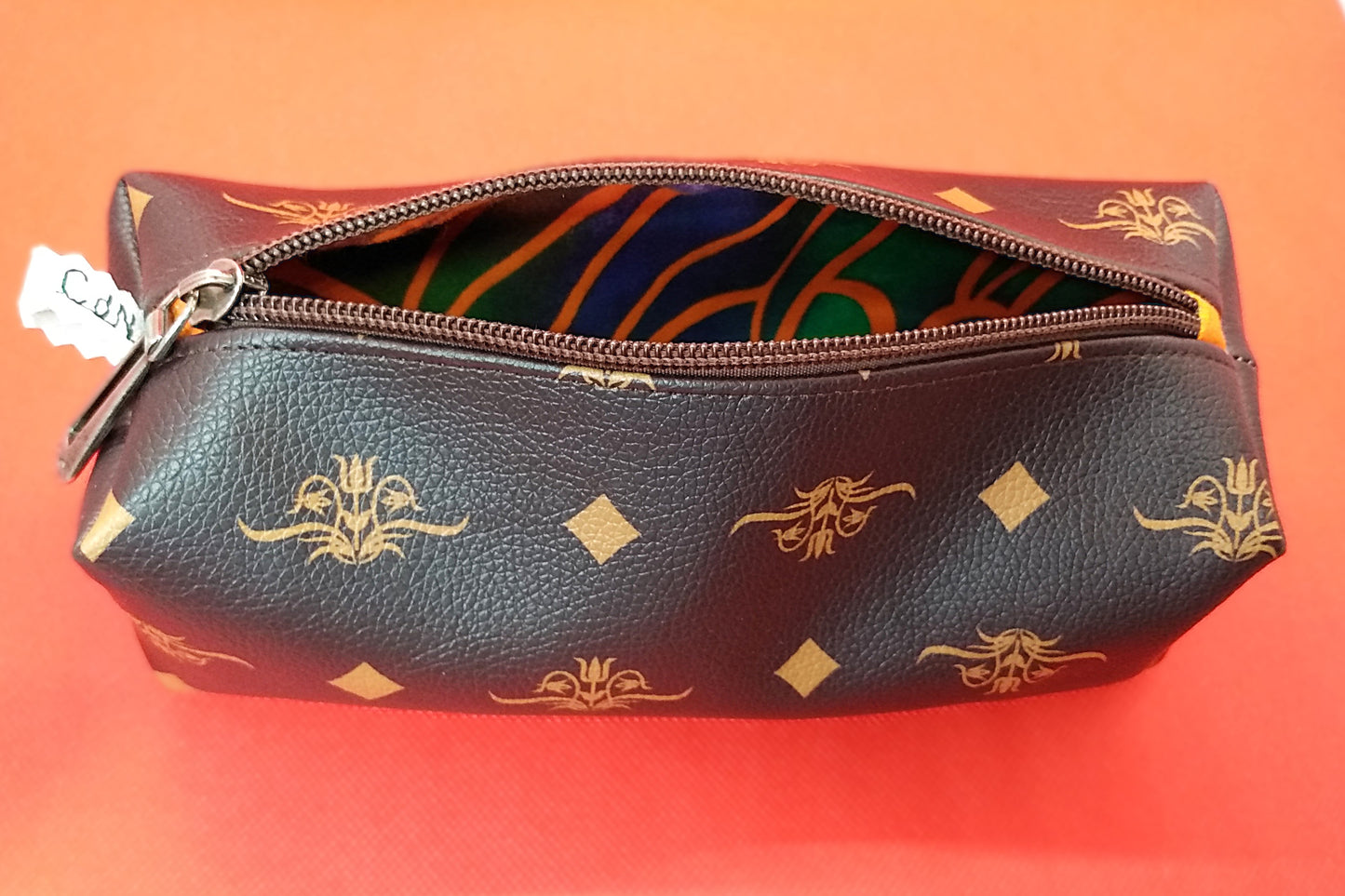 Trousse simili cuir marron à fleurs et losanges orangés. La trousse est ouverte et laisse apercevoir la doublure en tissu à motifs abstraits oranges sur fond vert et bleu foncés.