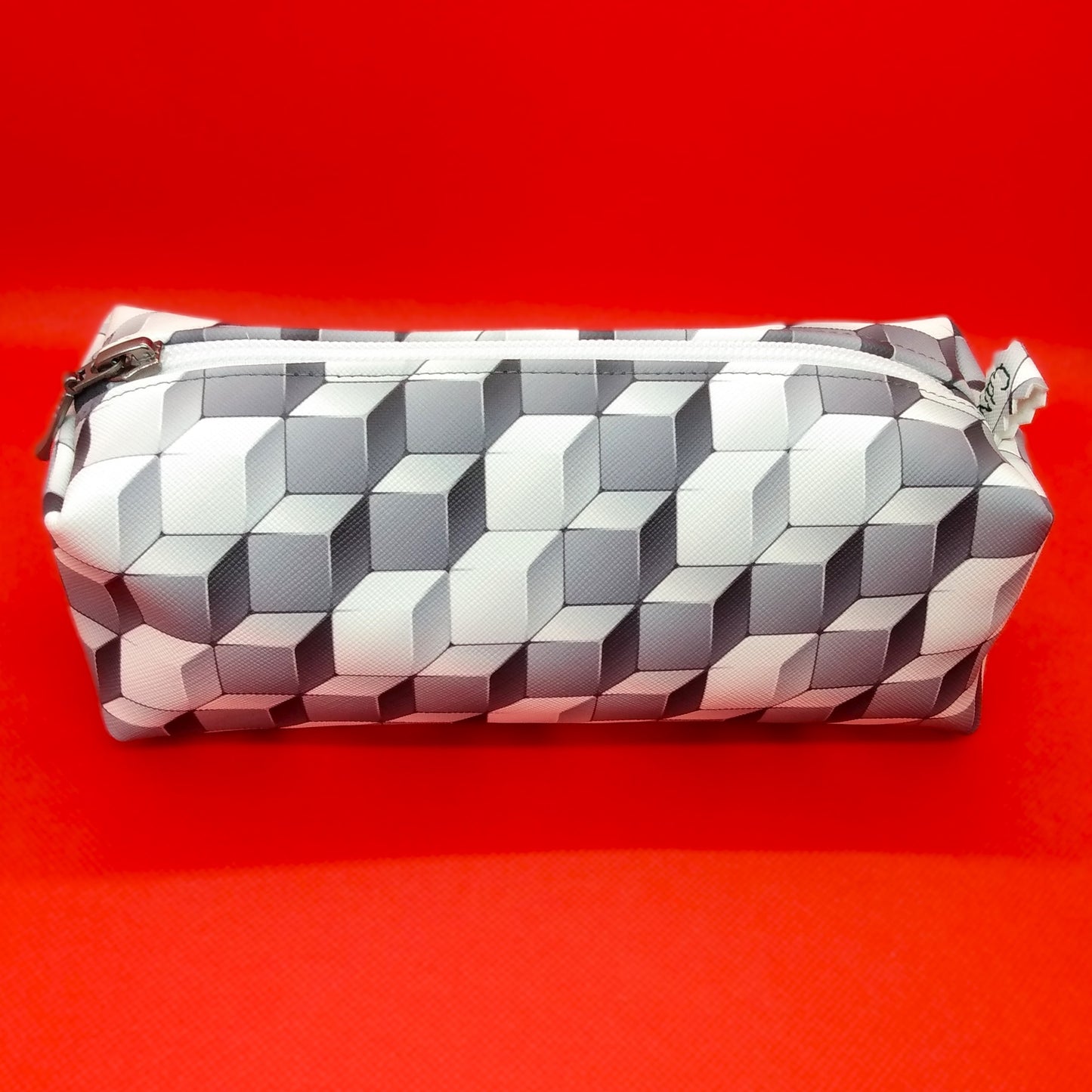 Trousse taille 1 simili cuir à motifs cubes gris et blancs. Se ferme par une fermeture éclair blanche. L'étiquette "CdN" de la marque est présente sur un côté de la trousse.
