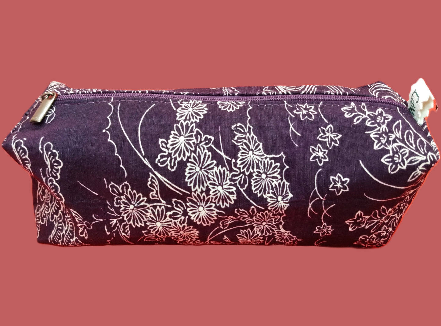 Trousse taille 1 tissu sur fond violet à motifs paysage fleuri blanc. Se ferme par une fermeture éclair violette. L'étiquette "CdN" de la marque est présente sur un côté de la trousse.