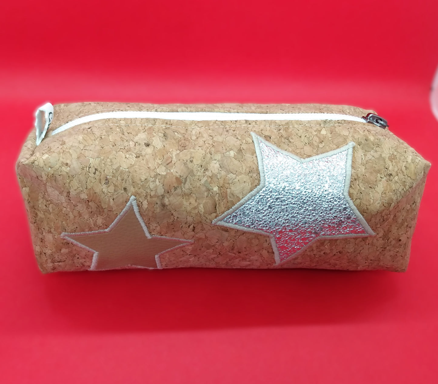 Trousse taille 1 en liège. Une grosse étoile argentée et une plus petite, en simili cuir beige, sont cousues sur le liège. Se ferme par une fermeture éclair blanche. L'étiquette "CdN" de la marque est présente sur un côté de la trousse.