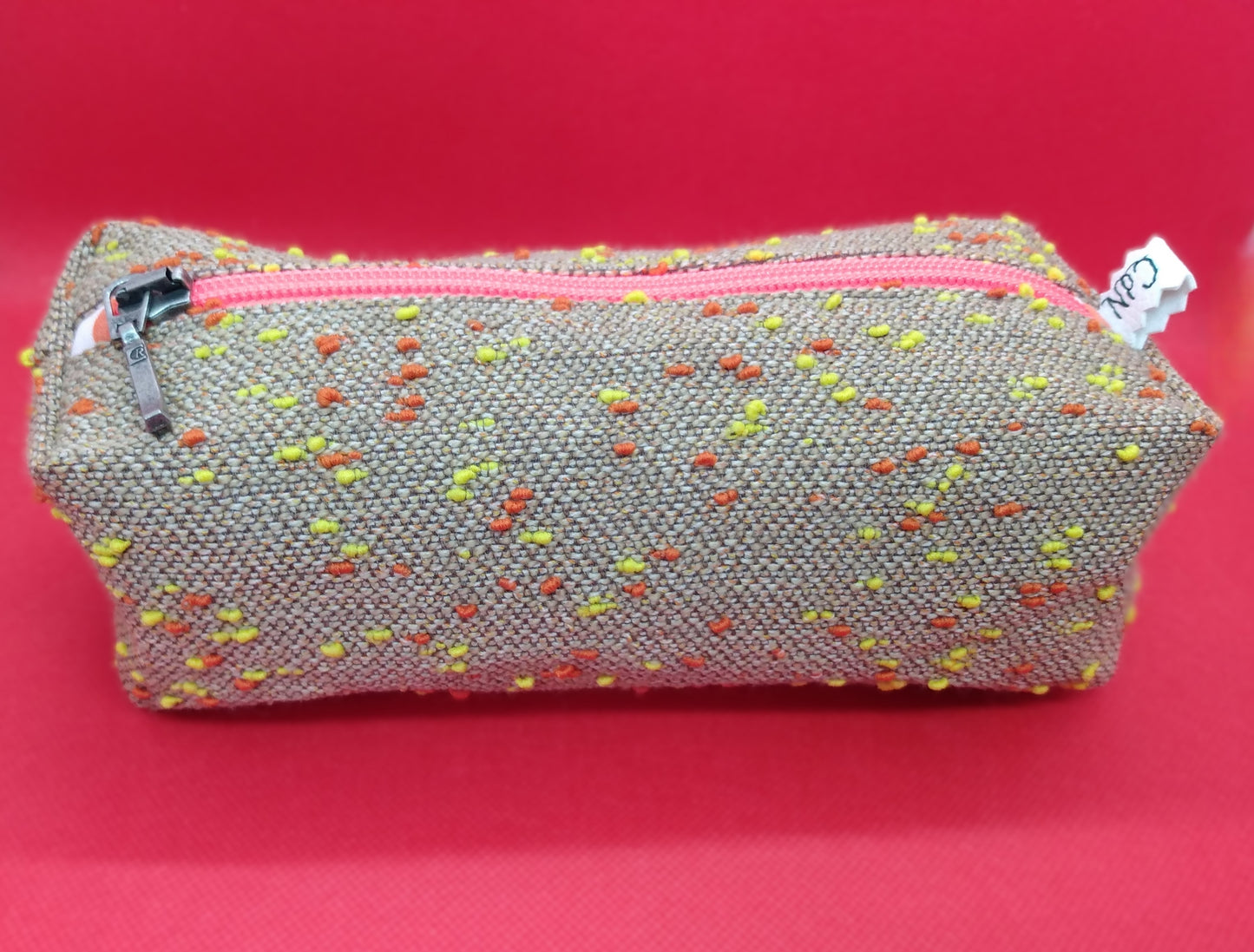 Trousse taille 1 étoffe tissée camel à petits pois oranges et jaunes. Se ferme par une fermeture éclair orange. L'étiquette "CdN" de la marque est présente sur un côté de la trousse.
