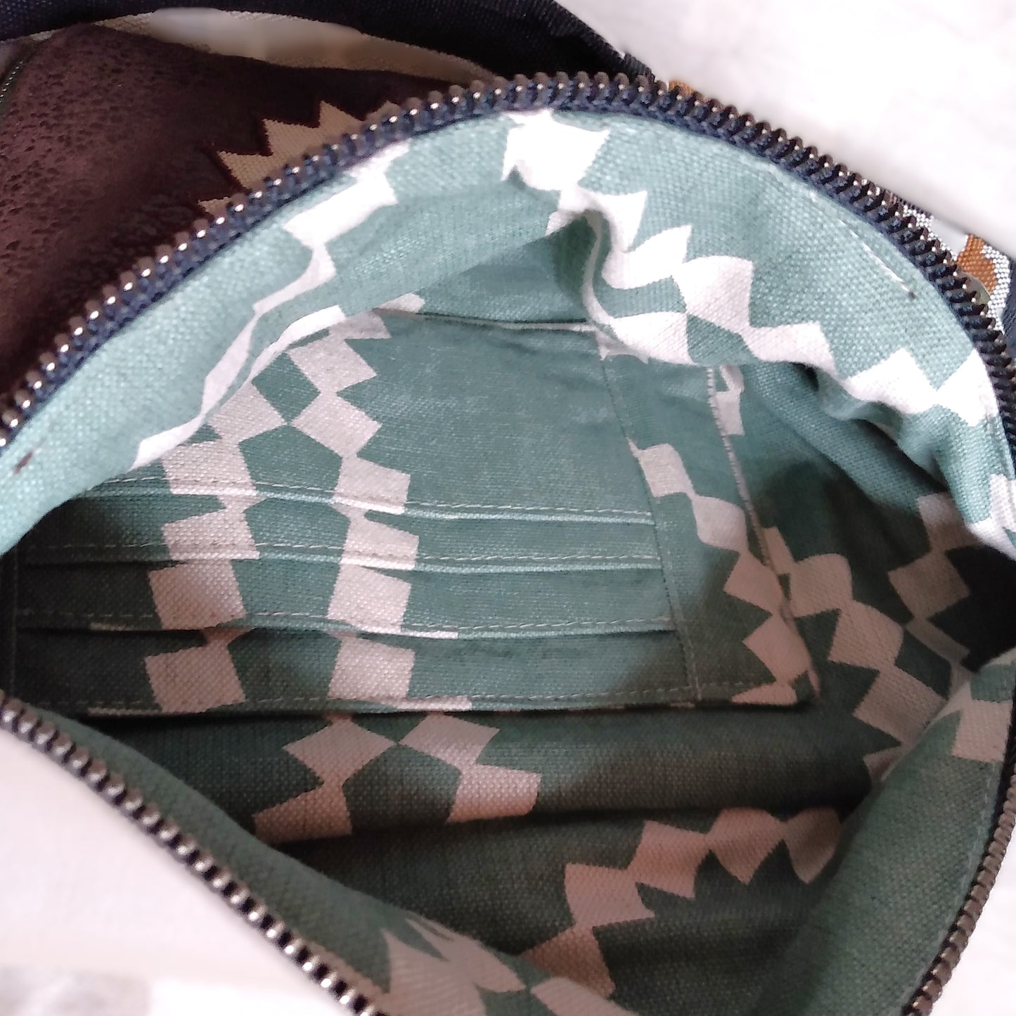 Intérieur du sac banane mango. On y voit une poche plaquée avec des compartiements à carte. Le tissu de doublure est de couleur verdé avec des motifs géométriques en forme de soleil beige.