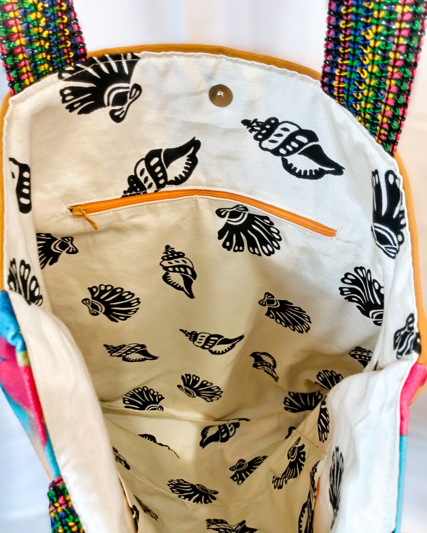 Intérieur du sac Ginger. Le tissu de doublure est beige avec de gros coquillages noirs. On voit une poche zippée à fermeture orange et un fermoir aimanté pour fermer le sac.