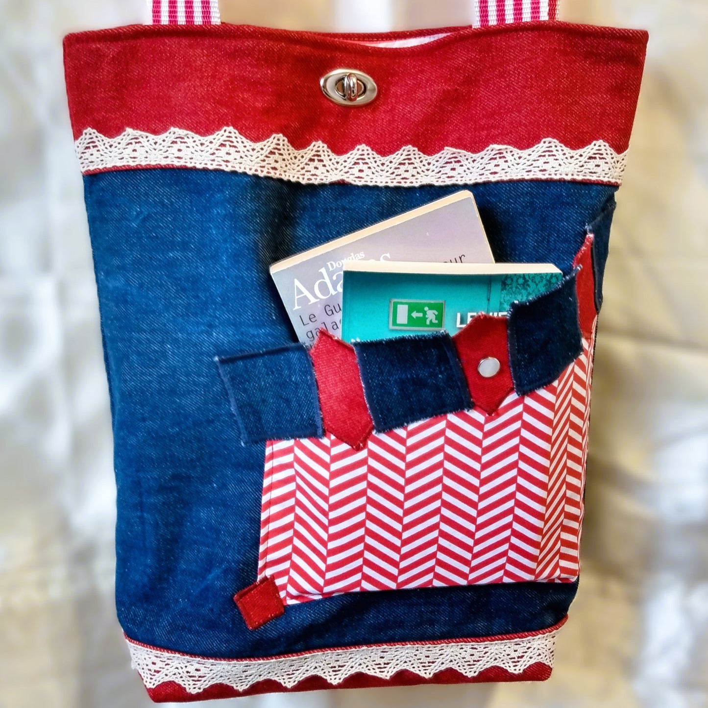 avant du sac Boujou. Couleurs principales, bleu, rouge et blanc. Extérieur en jean denim. Voir description détaillée sur la photo précédente. Seule différence avec l'autre photo, ici la poche avant contient deux livres de poche.