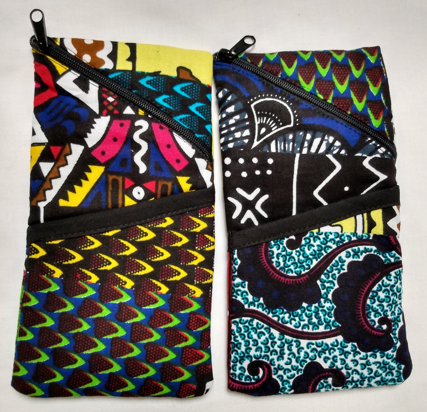 Étui à lunettes wax multicolore. Se ferme avec un zip noir. A l'extérieur, une poche ouverte, surmontée d'un biais noir est visible à l'avant, sur la moitié basse de l'étui.