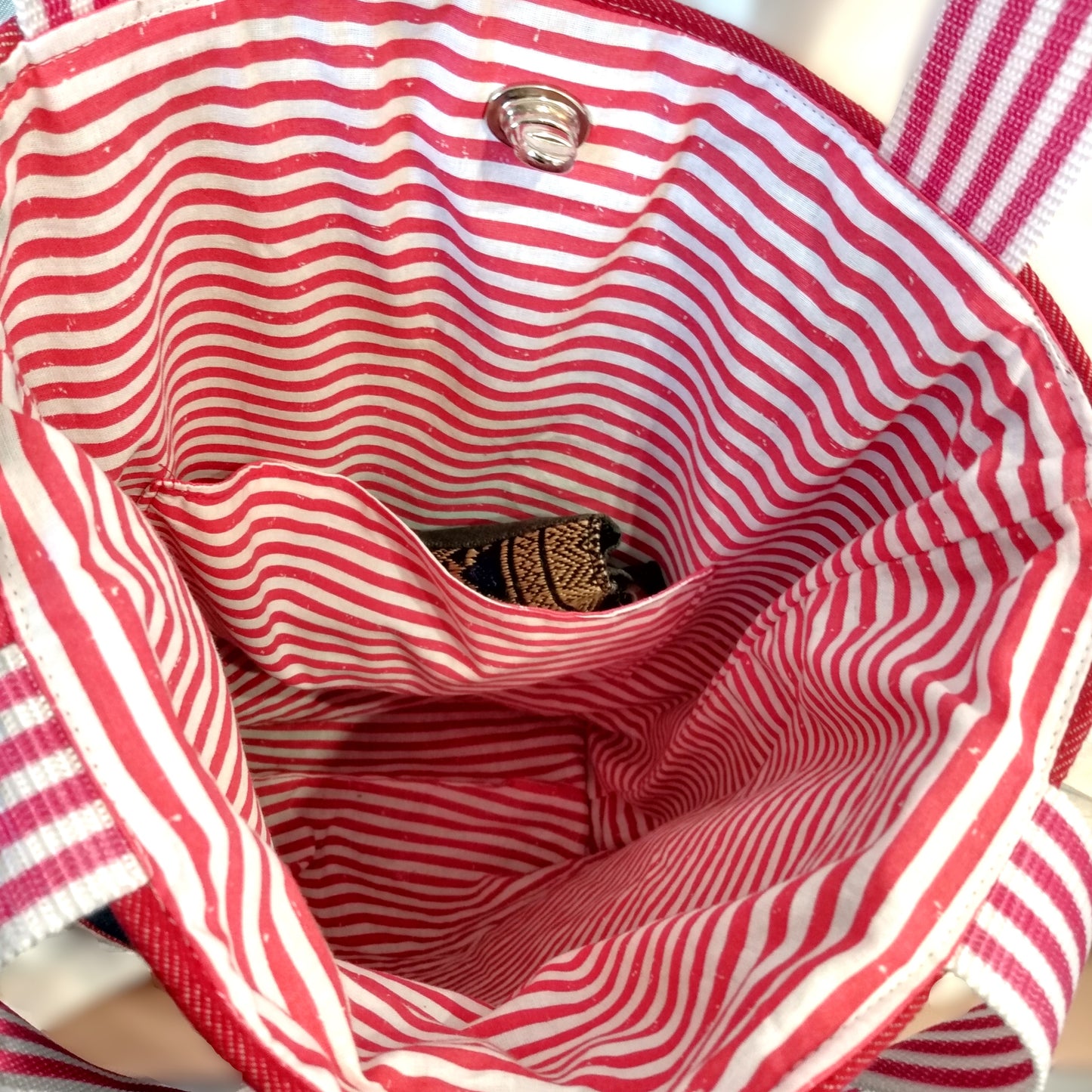 Intérieur du sac Boujou. Doublure en coton à rayures horizontales rouges et blanches. Une poche plaquée, avec un objet à l'intérieur, est visible dans le sac.