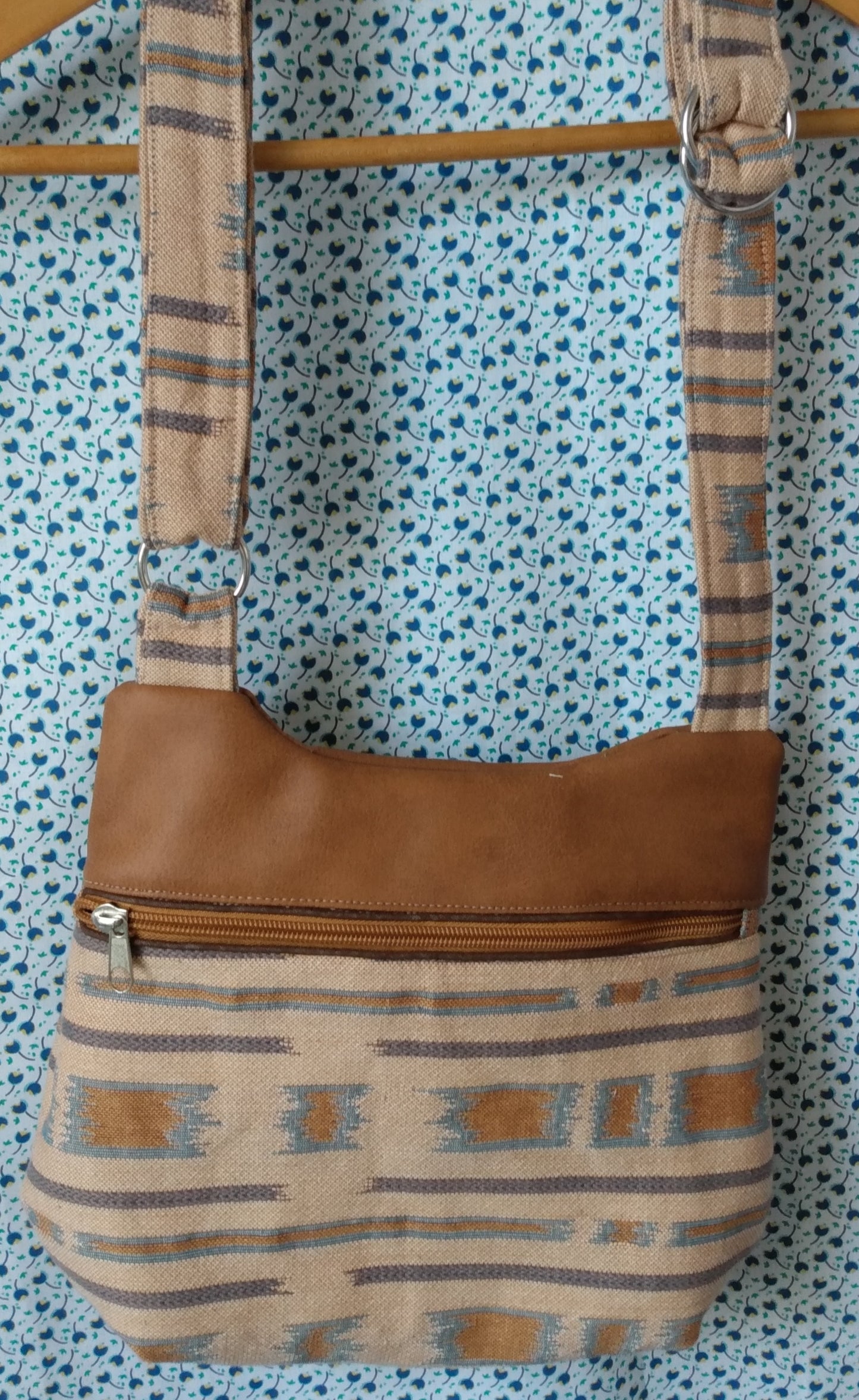 Vue avant du sac pivoine. L'anse et le bas du sac sont dans un tissu type jacquard beige avec des touches bleutées et marrons. Le haut du sac est en simili cuir marron. Le sac se ferme par une fermeture éclair marron. La bandoulière est réglable.