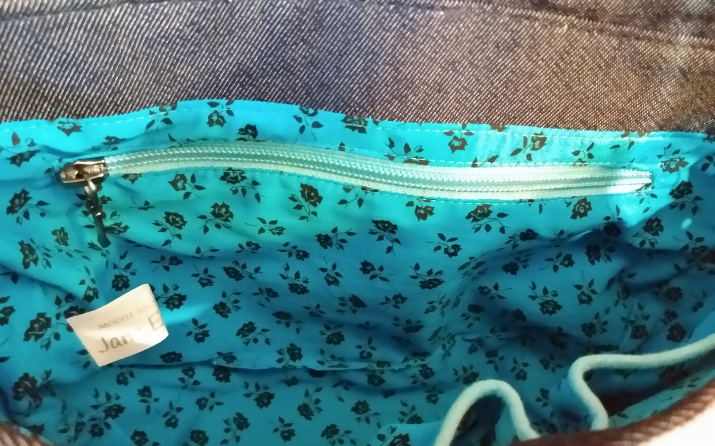 Vue intérieure arrière du sac Vegas jean. coton bleu clair à motif petites roses noires. Une poche zippée est visible. La fermeture éclair est bleu clair.