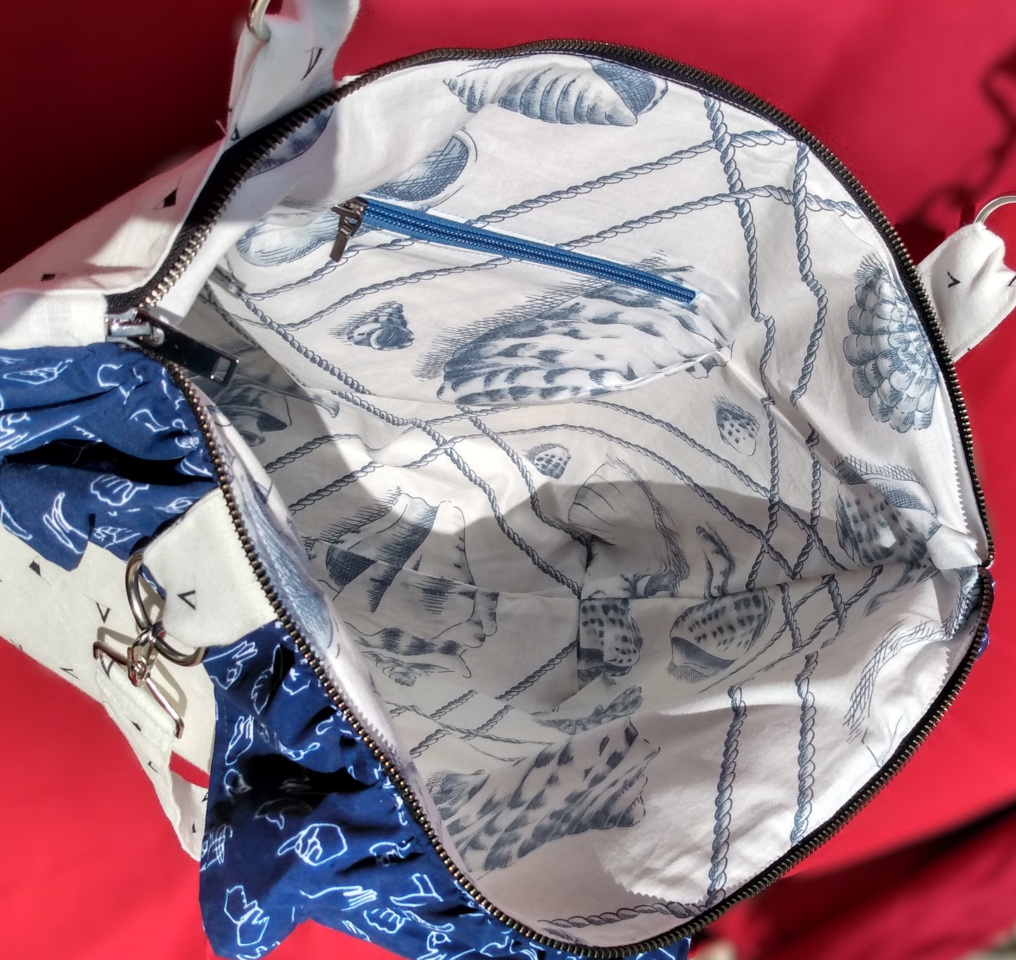 Intérieur du sac signora. La doublure est en coton blanc à motifs coquillages et cordes bleu gris. Une poche zippée est présente à l'intérieur du sac. Le zip est bleu clair.