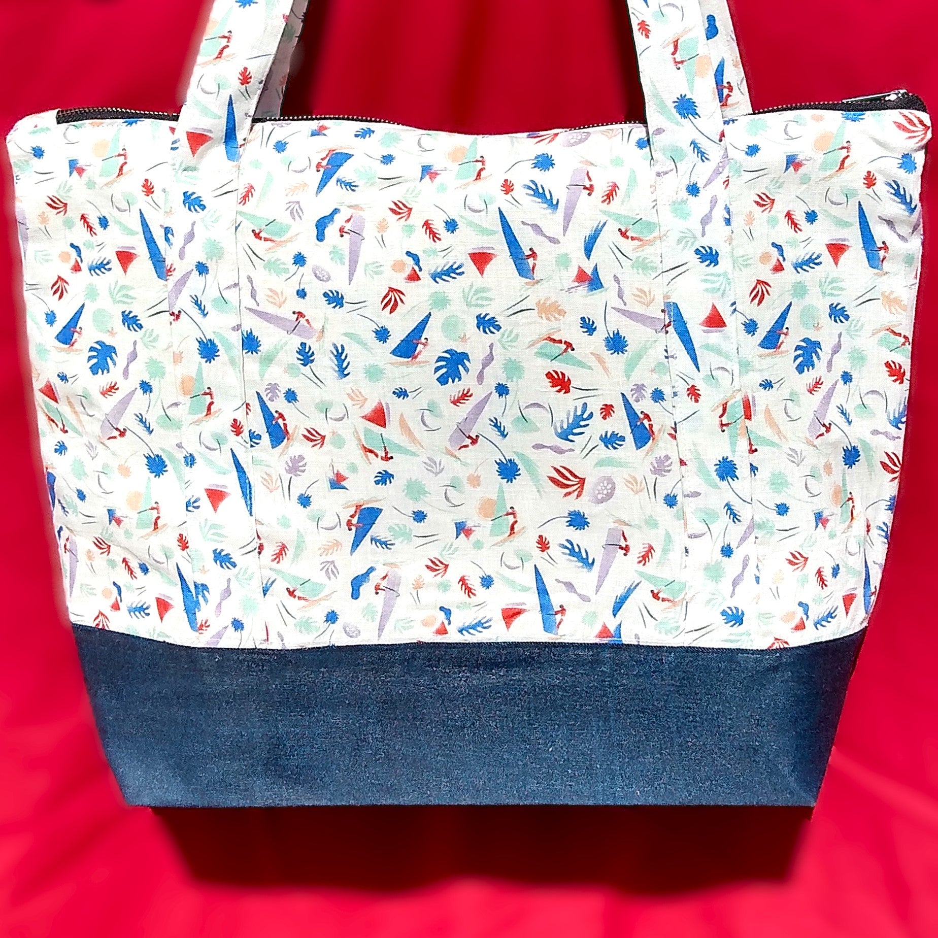 Avant du sac Bordemer. Le corps du sac est en lin beige à petits motifs feuilles et planches à voile  de plusieurs couleurs plutôt pastel. Le bas du sac est en jean. Les anses sont dans le même tissu que le corps du sac. Le sac se ferme avec une fermeture éclair métal.