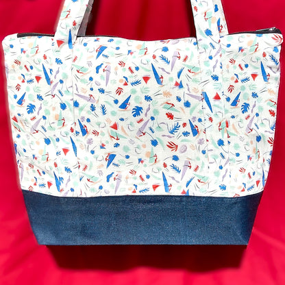 Avant du sac Bordemer. Le corps du sac est en lin beige à petits motifs feuilles et planches à voile  de plusieurs couleurs plutôt pastel. Le bas du sac est en jean. Les anses sont dans le même tissu que le corps du sac. Le sac se ferme avec une fermeture éclair métal.