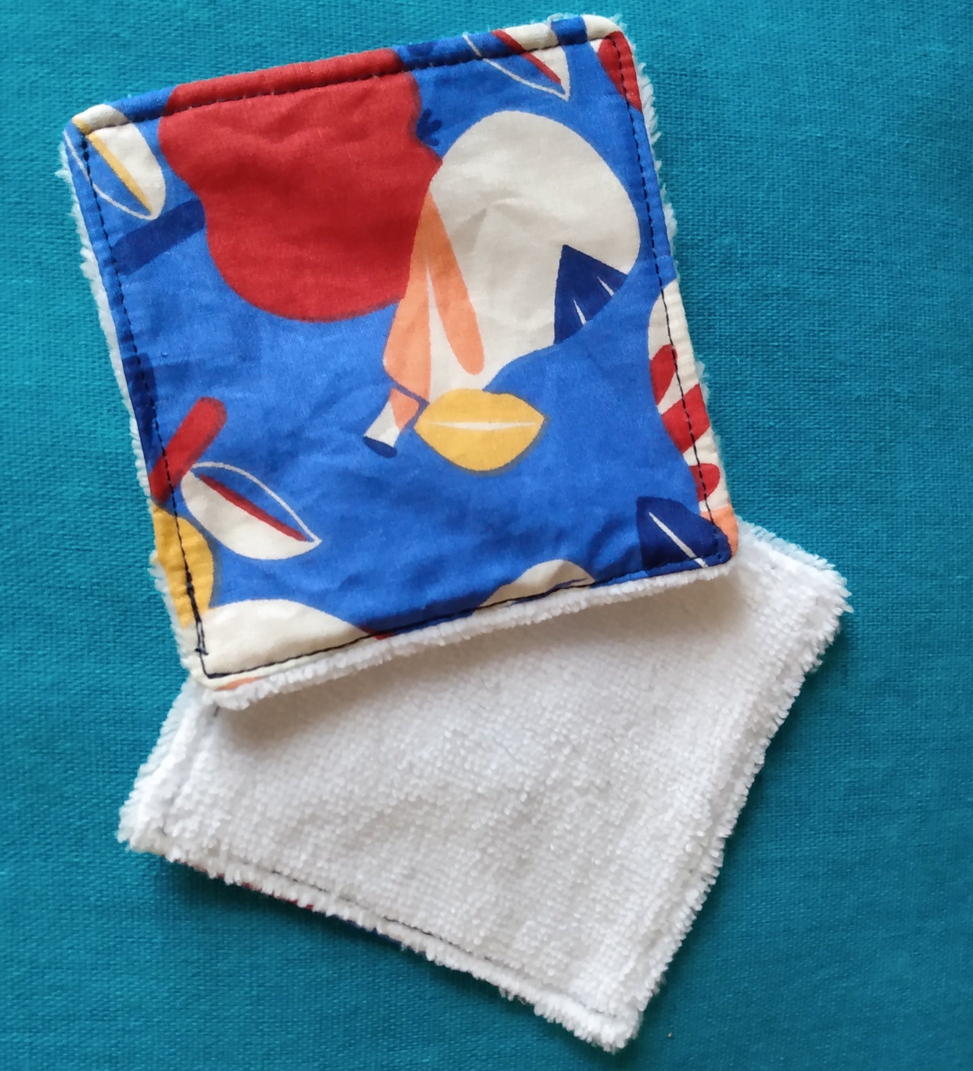 Lingettes démaquillantes carrées avec une face éponge blanche et une face en coton imprimé fruits avec dominante de couleurs bleu et rouge