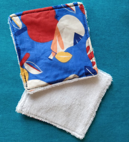 Lingettes démaquillantes carrées avec une face éponge blanche et une face en coton imprimé fruits avec dominante de couleurs bleu et rouge