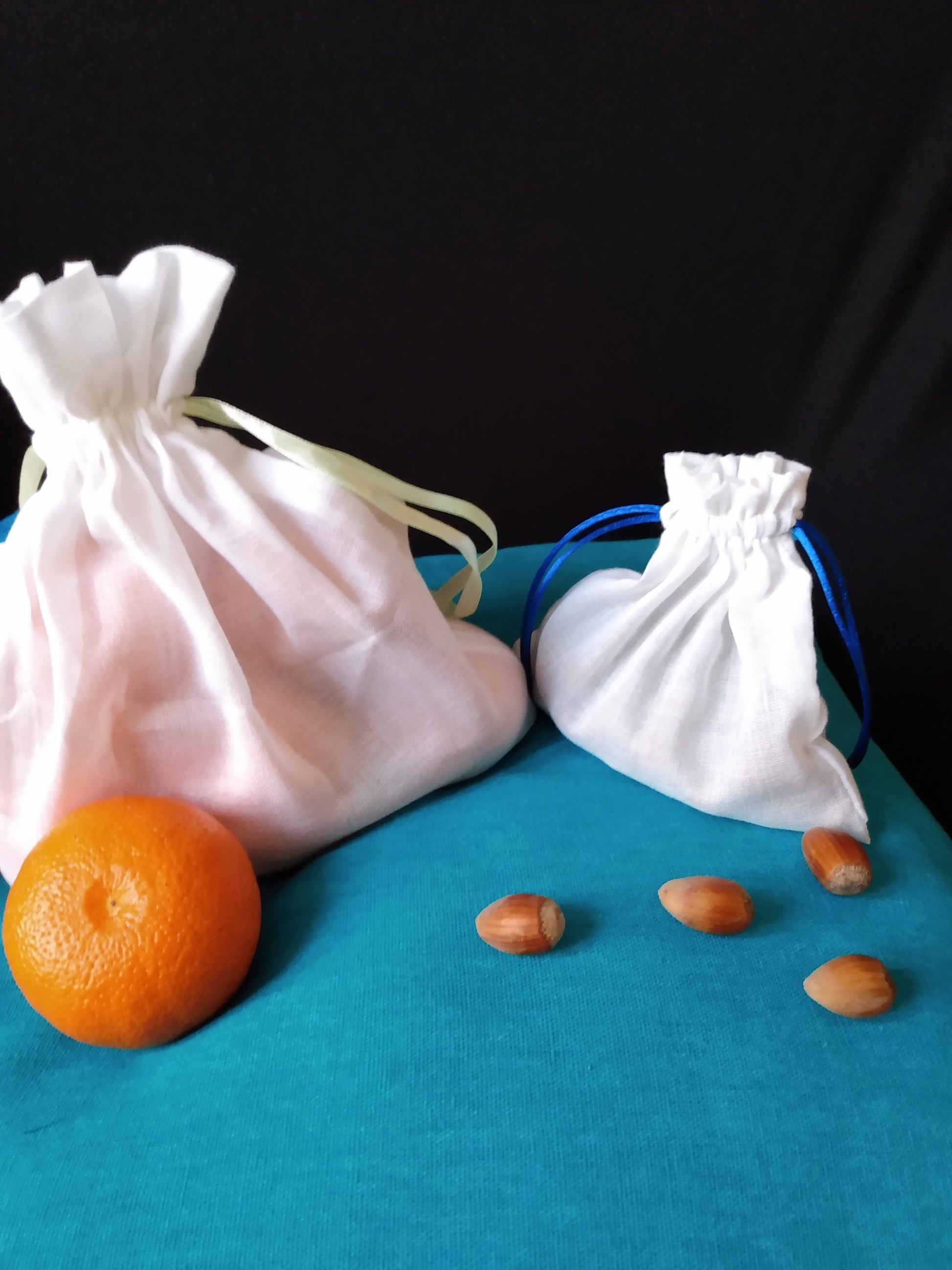 Un sac à vrac blanc de grande taille contenant des clémentines et un sac à vrac plus petit contenant des noisettes sont fermés et entourés de clémentines et de noisettes