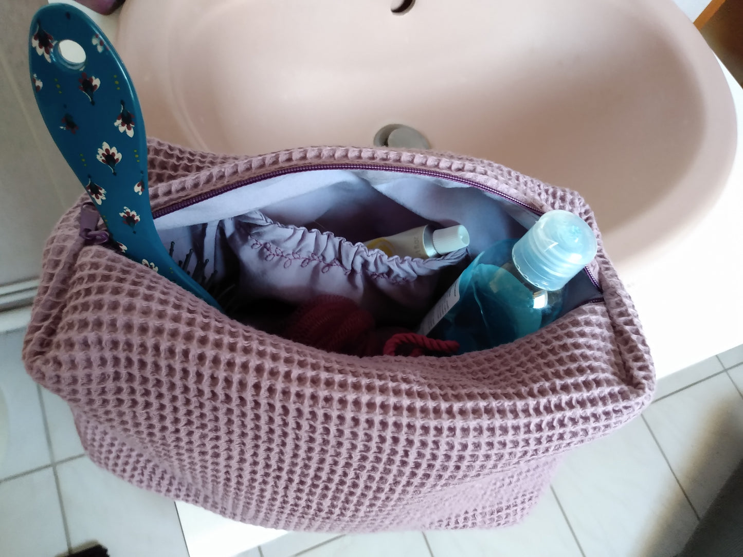 Trousse de toilette mauve avec de nombreux objets à l'intérieur et une poche intérieure élastiquée.