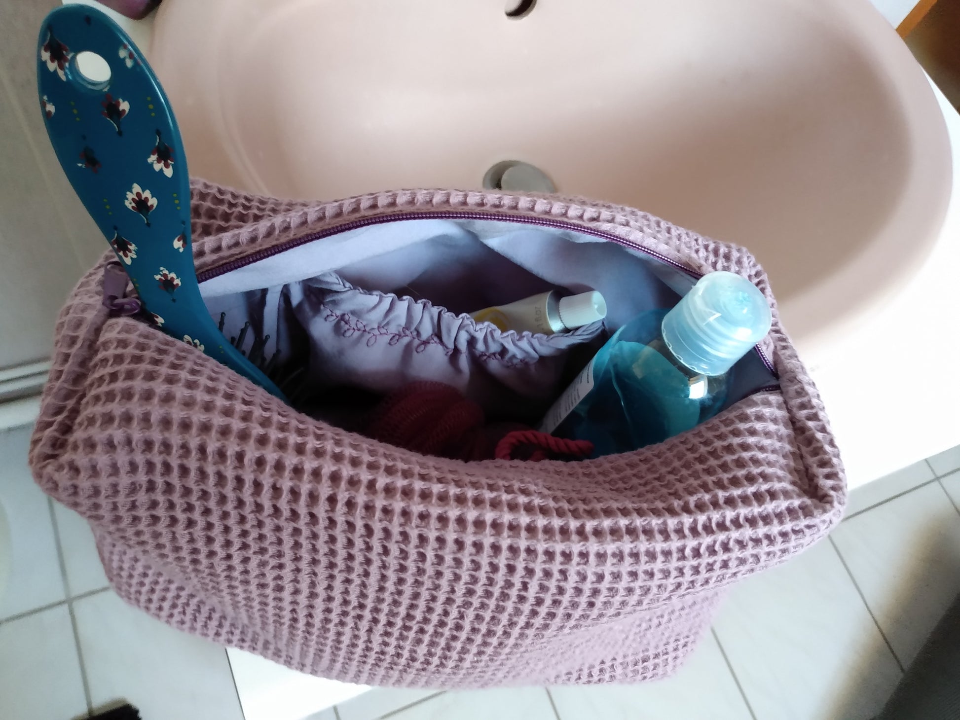 Trousse de toilette mauve avec de nombreux objets à l'intérieur et une poche intérieure élastiquée.