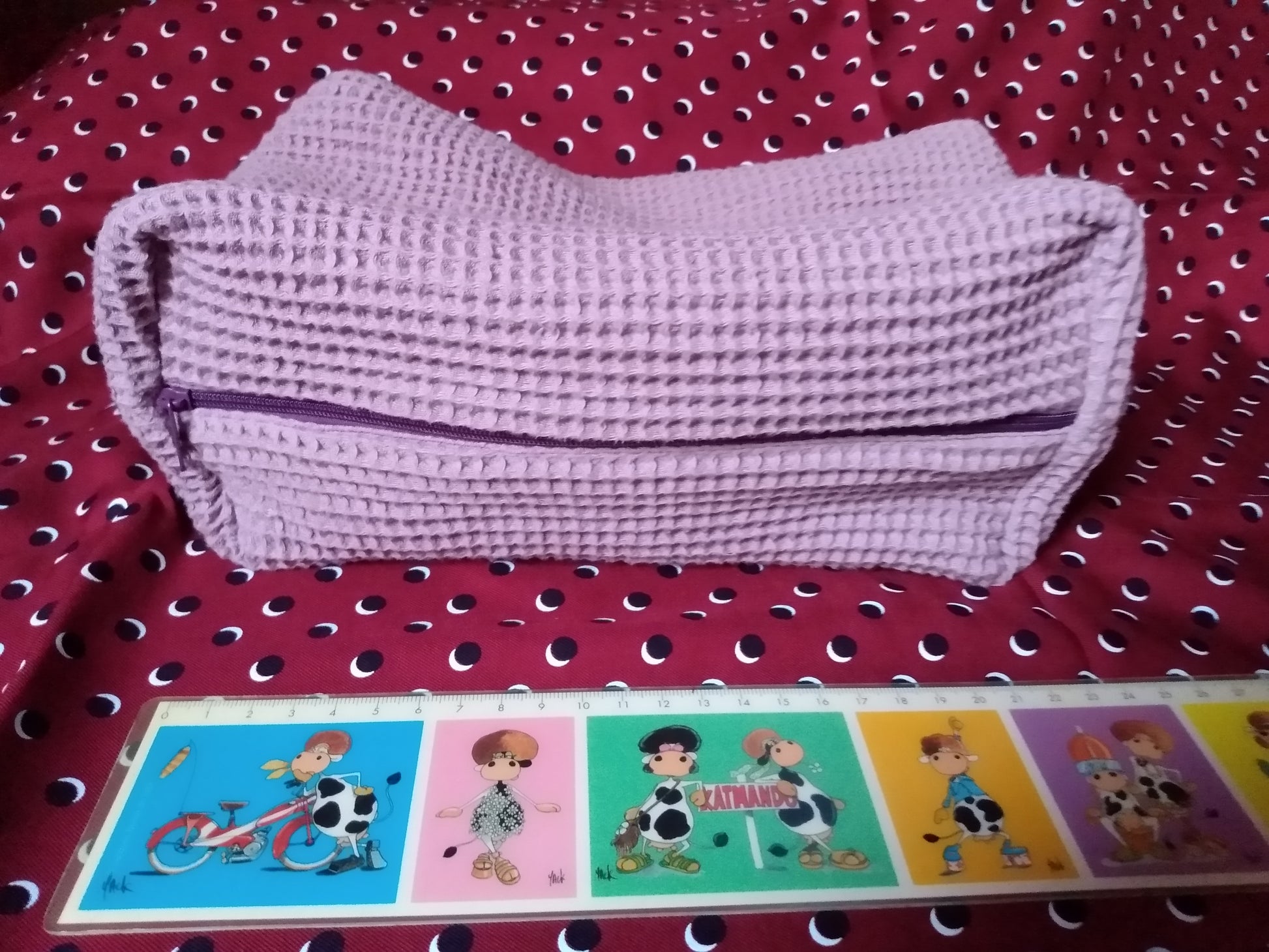 Trousse de toilette en tissu coton nid d'abeille mauve fermée avec une fermeture éclair. Elle mesure 25 cm de longueur.