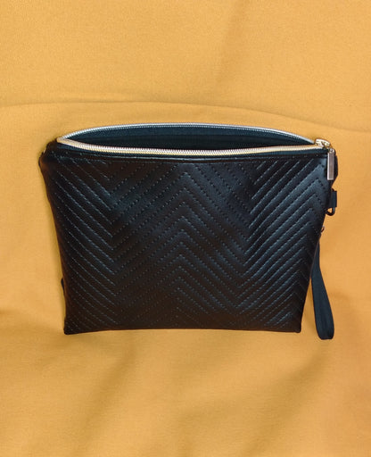 Arrière de la pochette Bonidé. Elle est en simili cuir noir à chevrons. On voit la dragonne noire sur le côté et la fermeture éclair ouverte laisse apercevoir la doublure en coton noire.