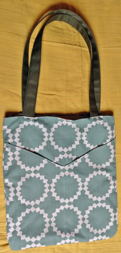 Avant du sac balad'in soleil vert. Le sac est en toile coton lin verdé avec des dessins géométriques  en forme de soleil beige. On voit 2 grandes poches plaquées dans le même tissu à l'avant.
Les anses sont en toile à sac kaki.