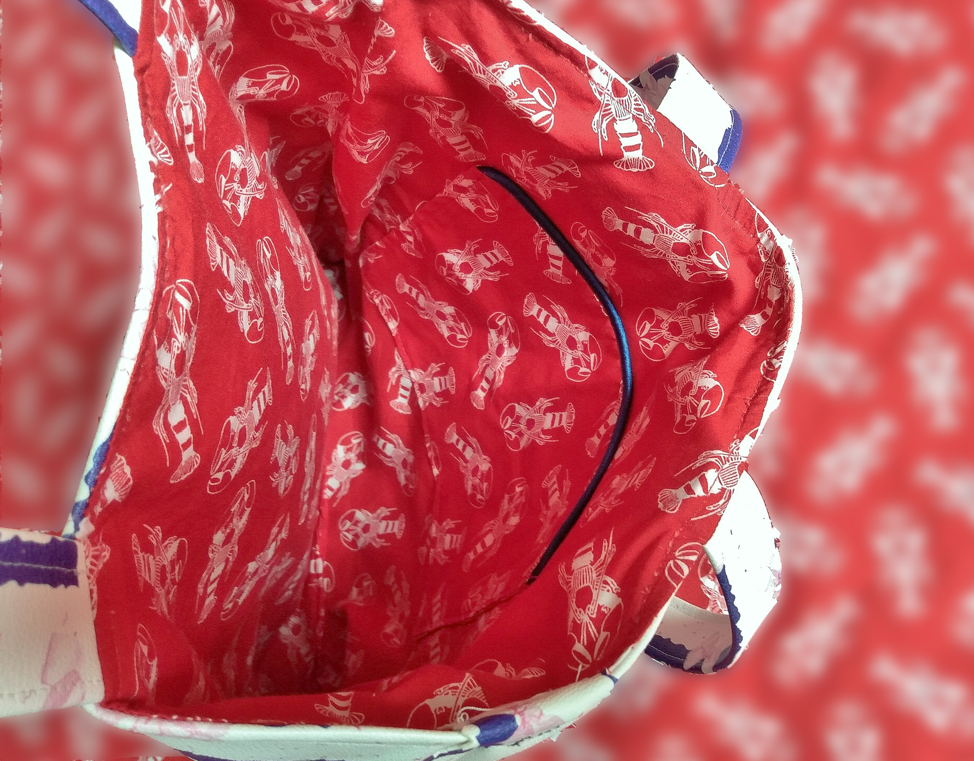 Intérieur du sac Jeanie. Le tissu est rouge avec des homards blancs. On voit une poche passepoilée à l'intérieur du sac.