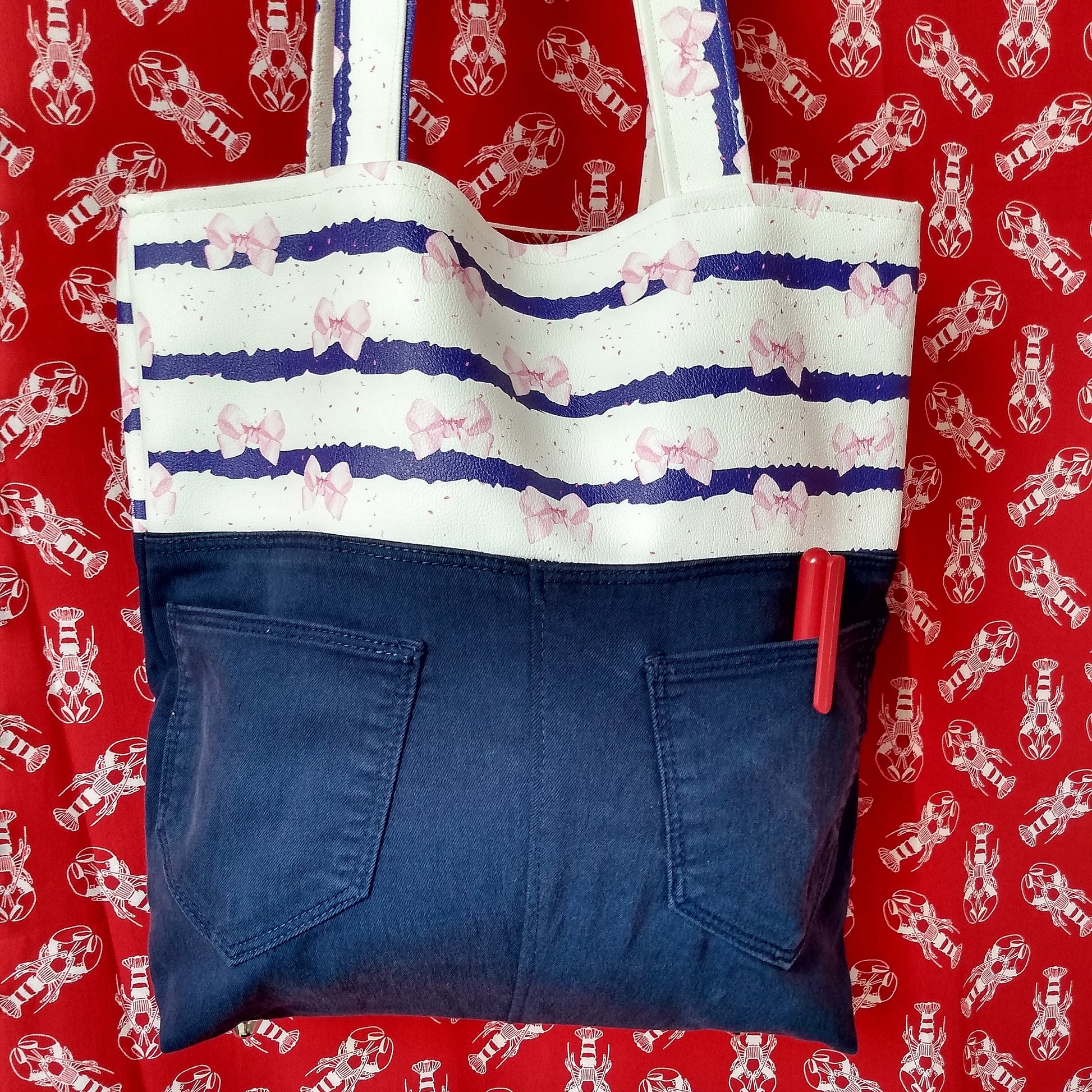Arrière du sac Jeanie. Le haut est dans le même simili cuir que le devant (rayé bleu et blanc avec noeuds roses). Le bas est fait en jean. on voit les deux poches arrières comme sur l'arrière d'un pantalon jean porté.