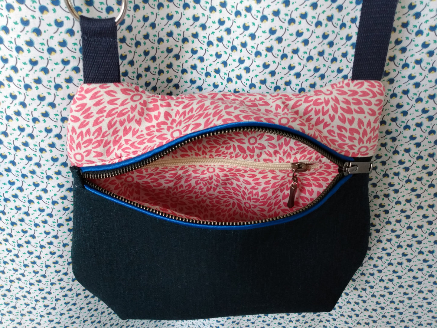 vue avant du sac pivoine bleu marine. Le zip est ouvert et laisse voir l'intérieur qui est doublé en coton beige à fleurs roses et possède une poche zippée.