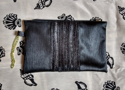 Vue avant pochette Soglad. 3 bandes verticales noires. La bande du milieu contient des paillettes. Une dragonne en chainette permet le port de la pochette au poignet. Une fermeture éclair ferme la pochette.