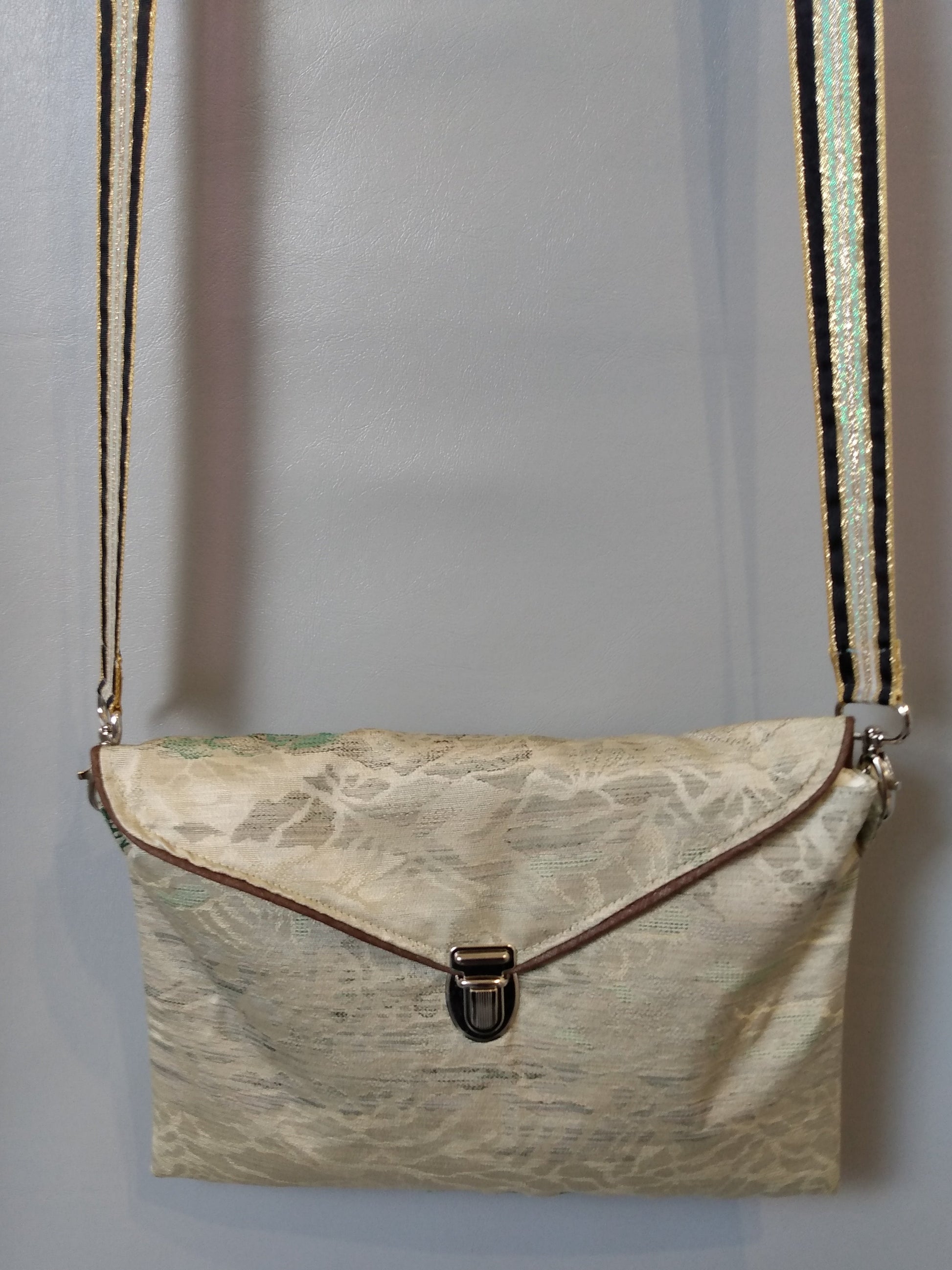 Avant de la pochette Kawa vert clair à motifs montagnes. Pochette se fermant par un rabat et une attache cartable nickelée. Le rabat est passepoilé (marron). Tissu extérieur tons verts à motif montagnes irisés.