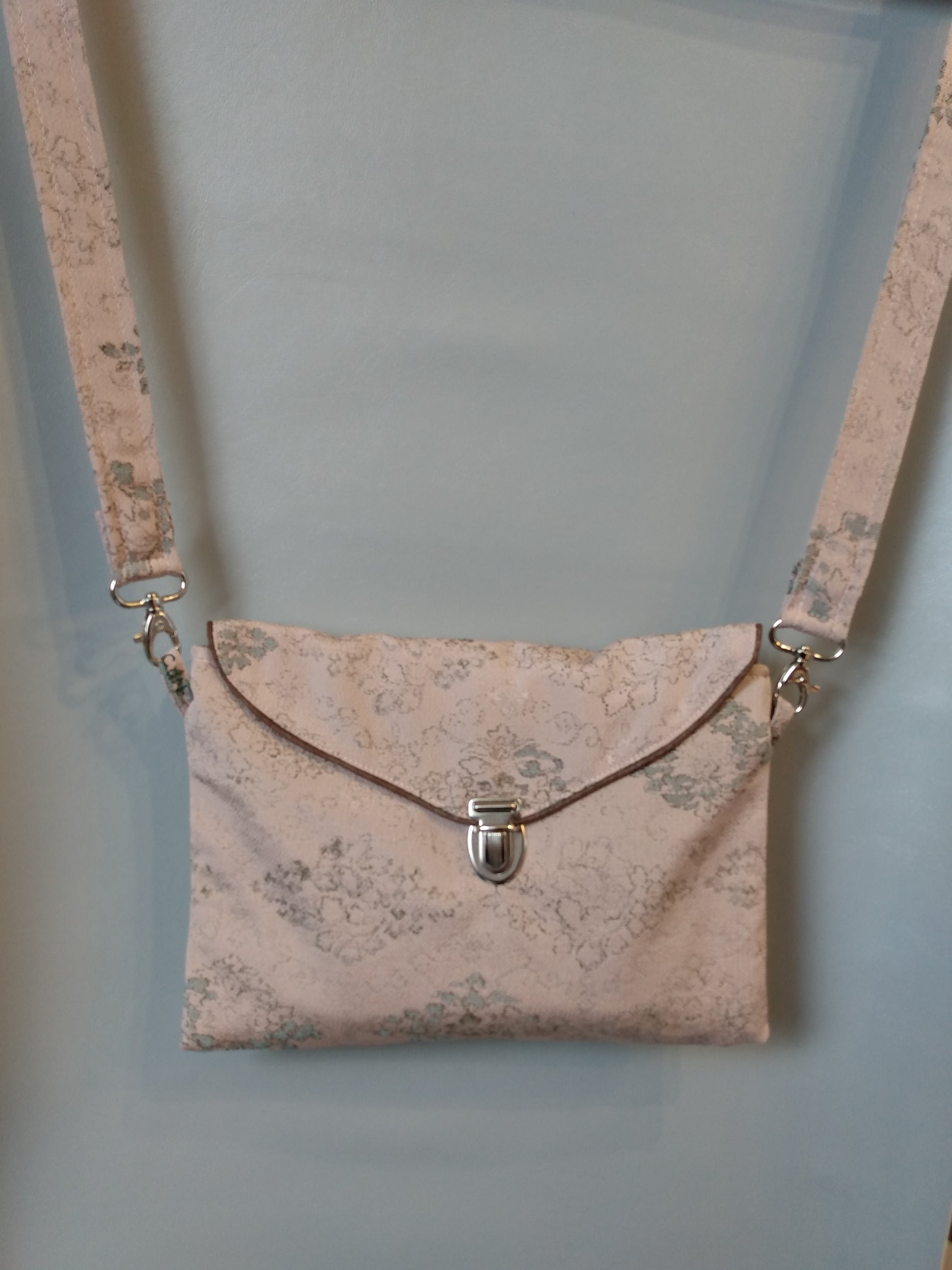 Avant de la pochette Kawa rose pâle.
Pochette se fermant par un rabat et une attache cartable nickelée. Le rabat est passepoilé (marron).
Le tissu extérieur est rose pâle à motifs floraux en losange.