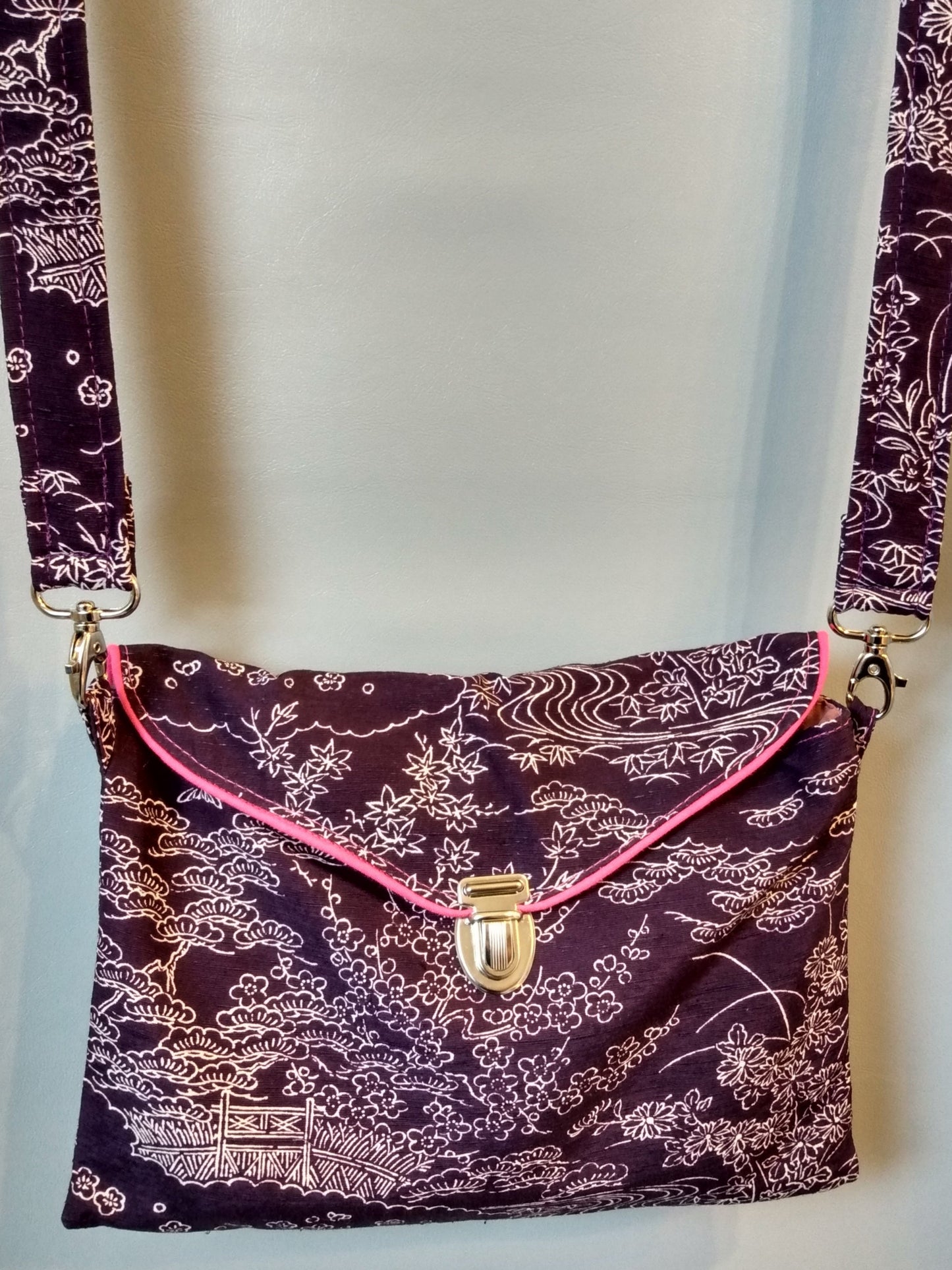 Avant de la pochette Kawa violette à motifs paysage.
Pochette se fermant par un rabat et une attache cartable nickelée. Le rabat est passepoilé (rose).
Tissu extérieur paysage blanc sur fond violet.