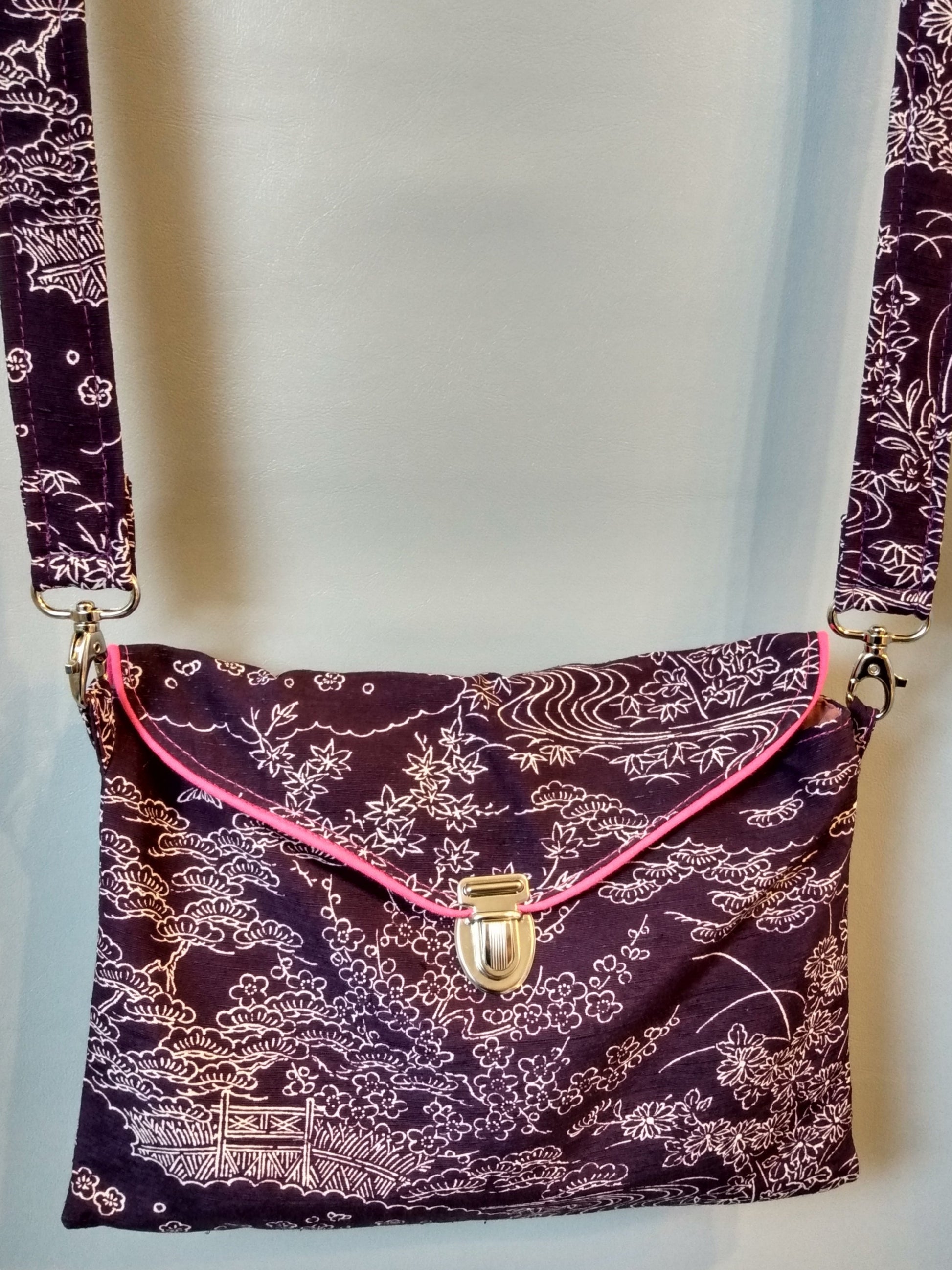 Avant de la pochette Kawa violette à motifs paysage.
Pochette se fermant par un rabat et une attache cartable nickelée. Le rabat est passepoilé (rose).
Tissu extérieur paysage blanc sur fond violet.
