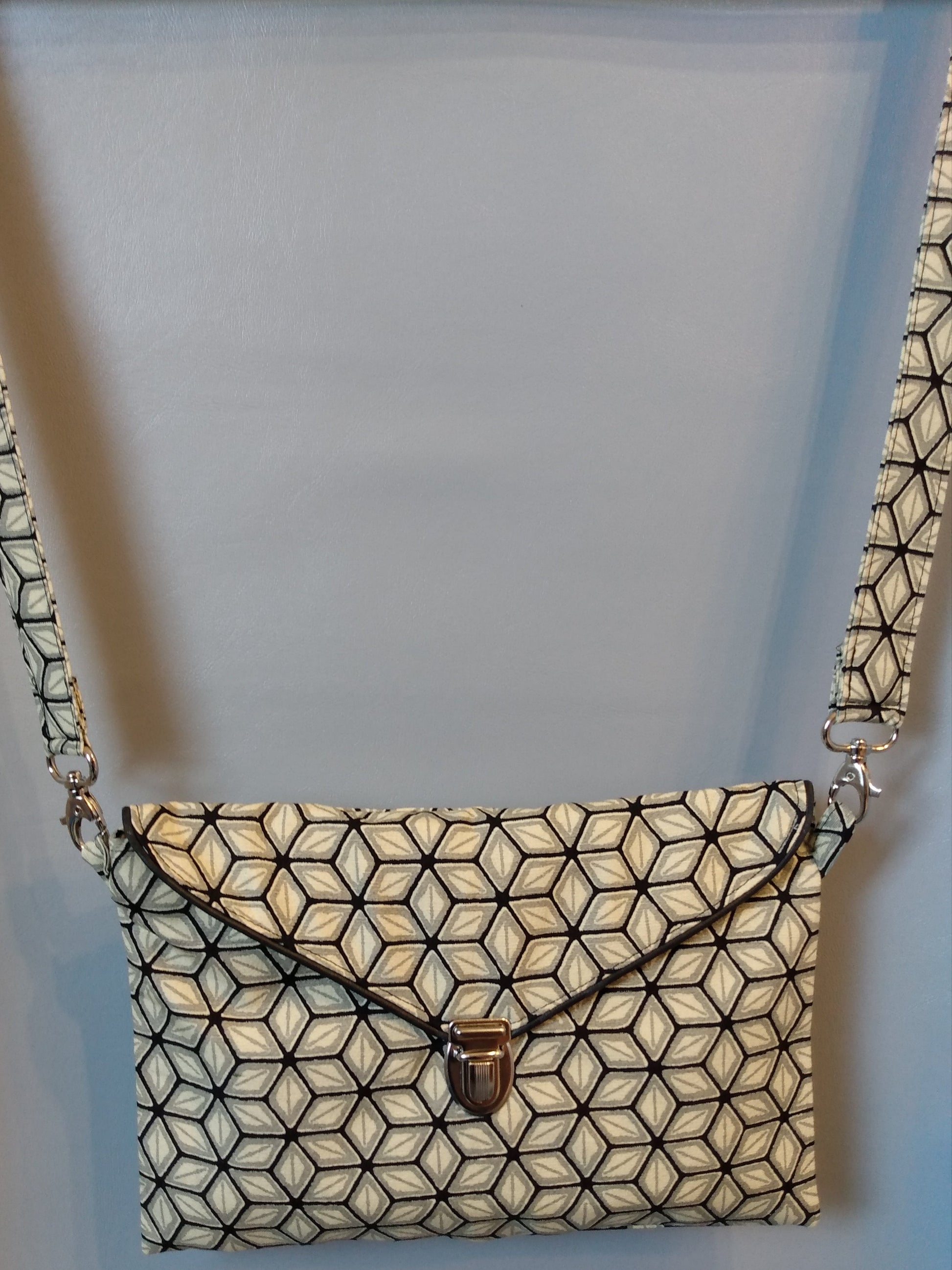 Avant de la pochette Kawa  étoile beige gris et noir.
Pochette se fermant par un rabat et une attache cartable nickelée. Le rabat est passepoilé (noir). Tissu extérieur et bandoulière motif étoile beige gris et noir.