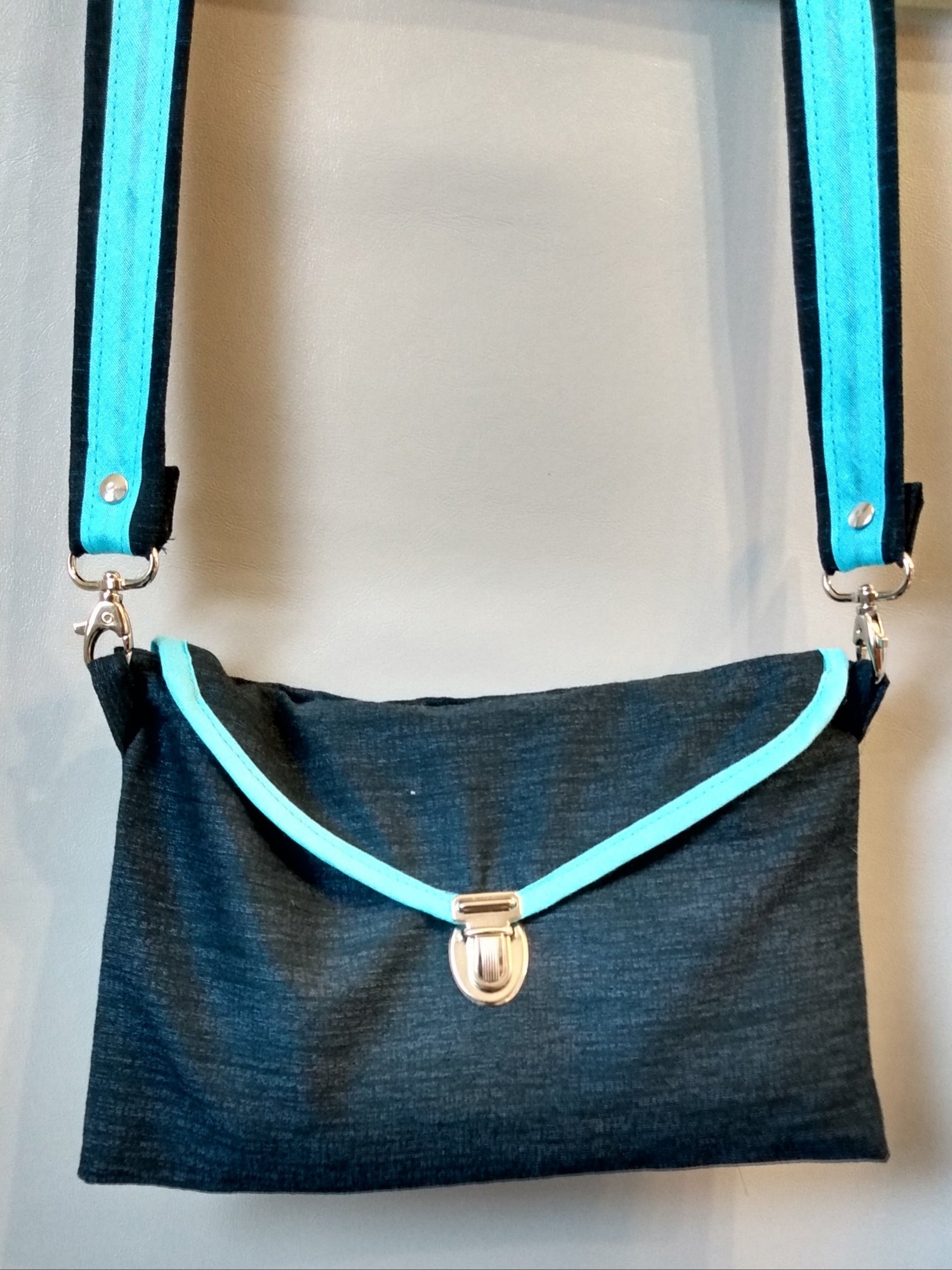 Avant de la pochette Kawa bleu marine.
Tissu bleu marine se fermant par un rabat et une attache cartable nickelée. Le rabat est entouré d'un biais bleu clair. La bandoulière est bicolore bleu marine et bleu clair.
