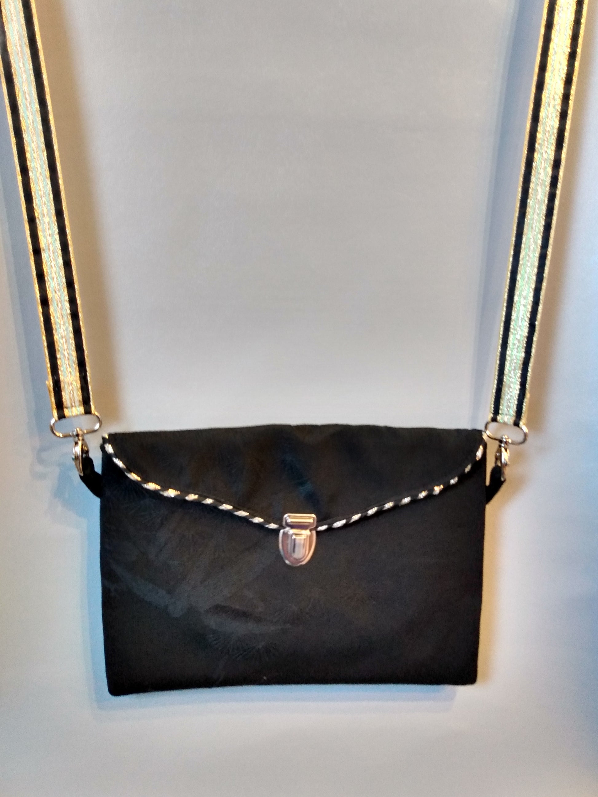 Avant de la pochette Kawa noir.
Pochette se fermant par un rabat et une attache cartable nickelée. Le rabat est passepoilé (or et noir). Tissu extérieur noir à motifs plantes noirs brodés.