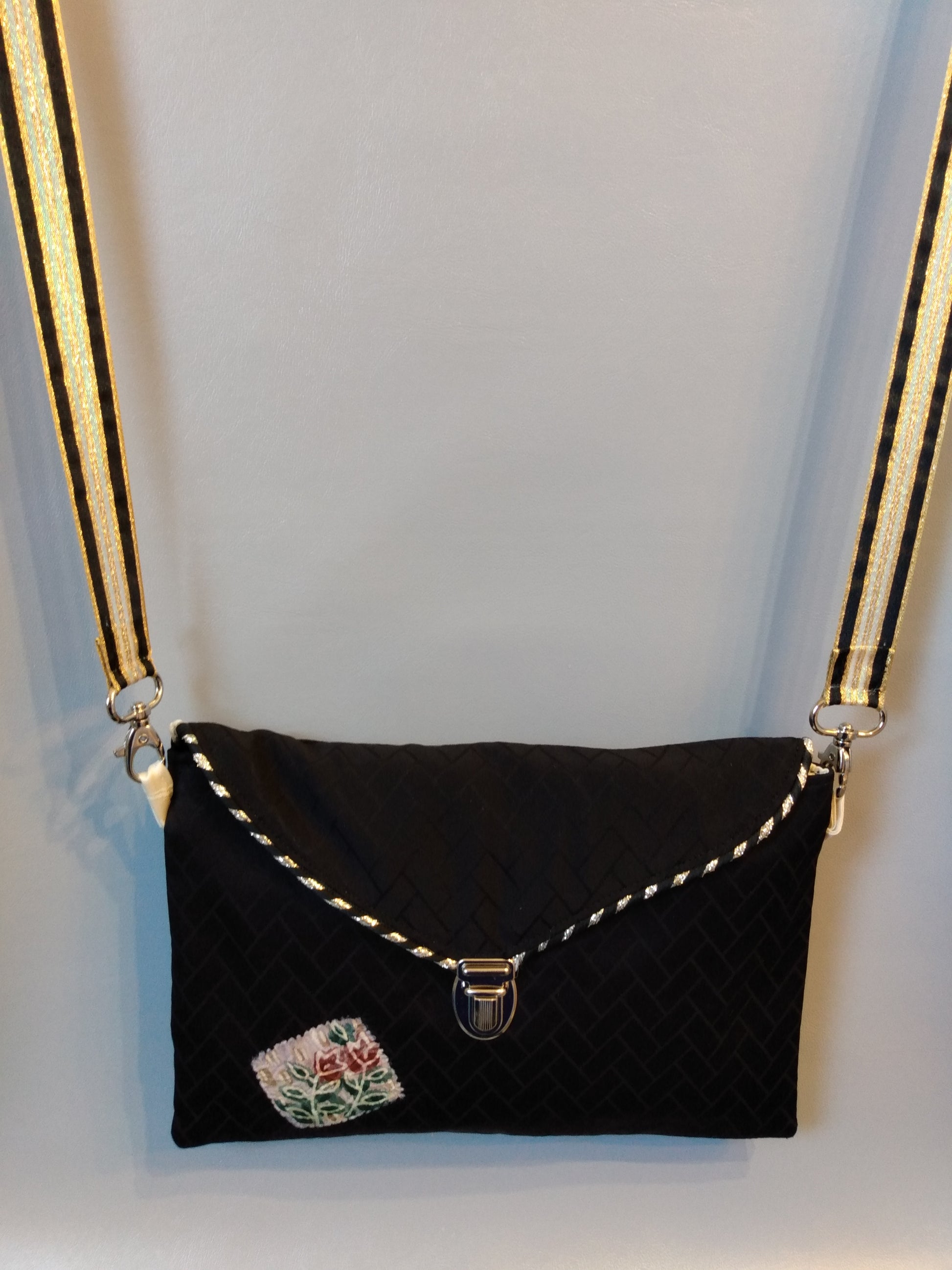 Avant de la pochette Kawa noir motifs géométriques.
Pochette se fermant par un rabat et une attache cartable nickelée. Le rabat est passepoilé (or et noir).
Tissu extérieur noir à motifs géométriques noir et beige.
