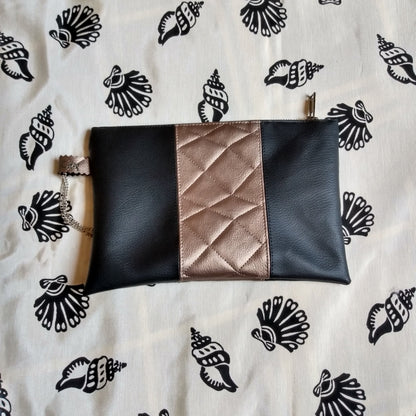 Vue avant pochette Soglad. 3 bandes simili cuir verticales : noir, doré effet matelassé et noir. Une dragonne en chainette permet le port de la pochette au poignet. Une fermeture éclair ferme la pochette.