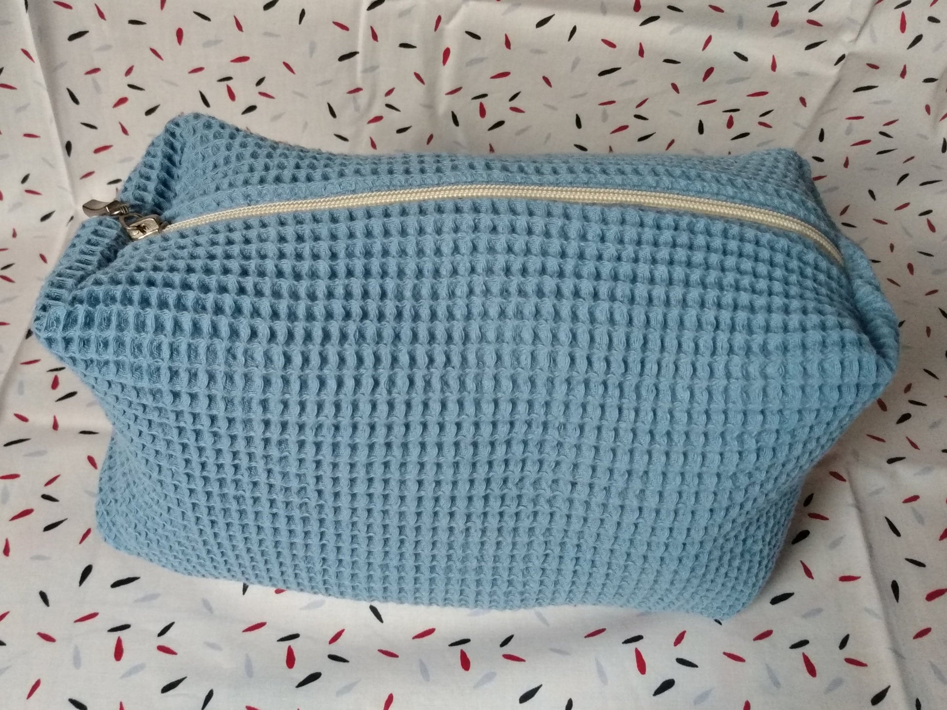 Trousse de toilette en coton nid d'abeille bleu clair, vue extérieure. Se ferme avec un zip (ici, beige avec un curseur métal).