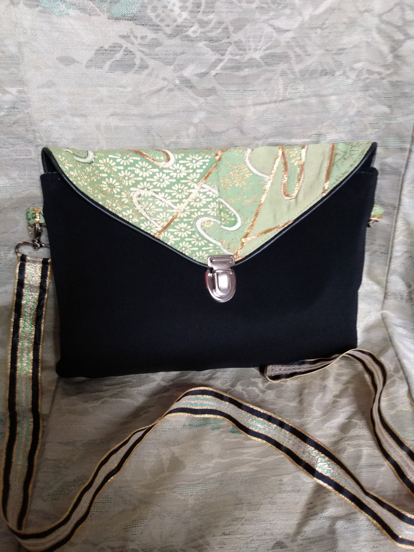 Pochette Kawa vue de devant. Pochette à rabat se fermant avec un fermoir cartable. Anse permet le port en bandoulière ou à l'épaule.