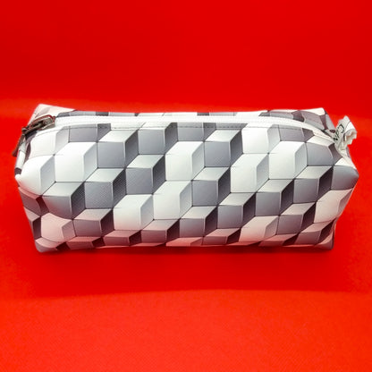 Trousse taille 1 simili cuir à motifs cubes gris et blancs. Se ferme par une fermeture éclair blanche. L'étiquette "CdN" de la marque est présente sur un côté de la trousse.