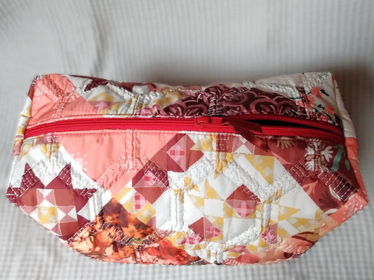 Trousse de toilette Flamingo. Vue du dessus. Cette trousse de toilette est rectangulaire, elle se ferme avec une fermeture éclair rouge. L'extérieur est en tissu matelassé imprimé en patchwork dans les tons roses, bordeaux, blanc...