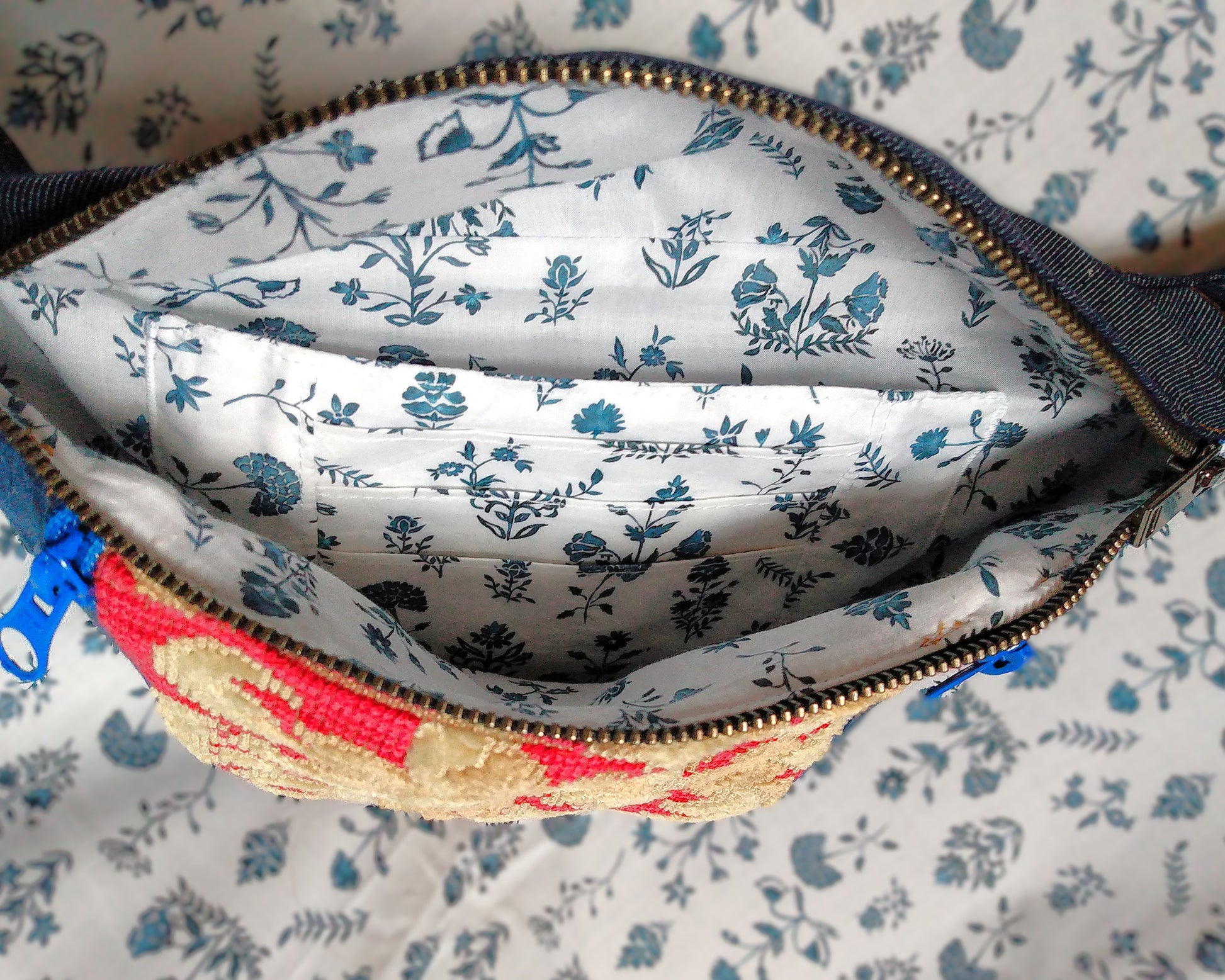 Intérieur du sac Mango. Le tissu de doublure est blanc avec des fleurs bleues. On voit une poche plaquée faisant également porte carte (3 étages de cartes). Ce grand compartiment principal de la banane se ferme avec une fermeture éclair métal.