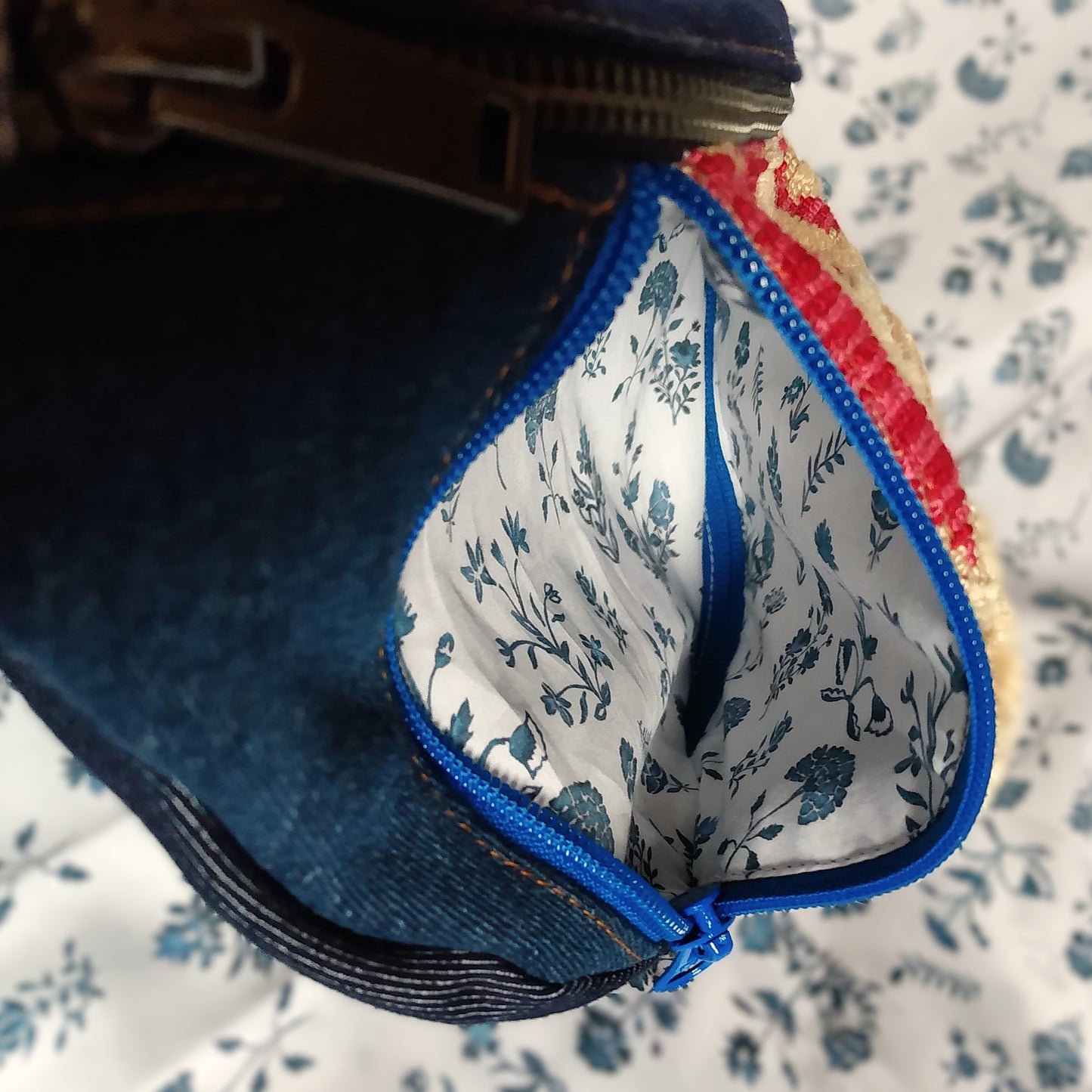 Intérieur de la poche avant du sac Mango. La fermeture éclair bleue droite est ouverte et laisse apercevoir la doublure de la poche blanche à fleurs bleues. On aperçoit au fond, la fermeture gauche fermée.