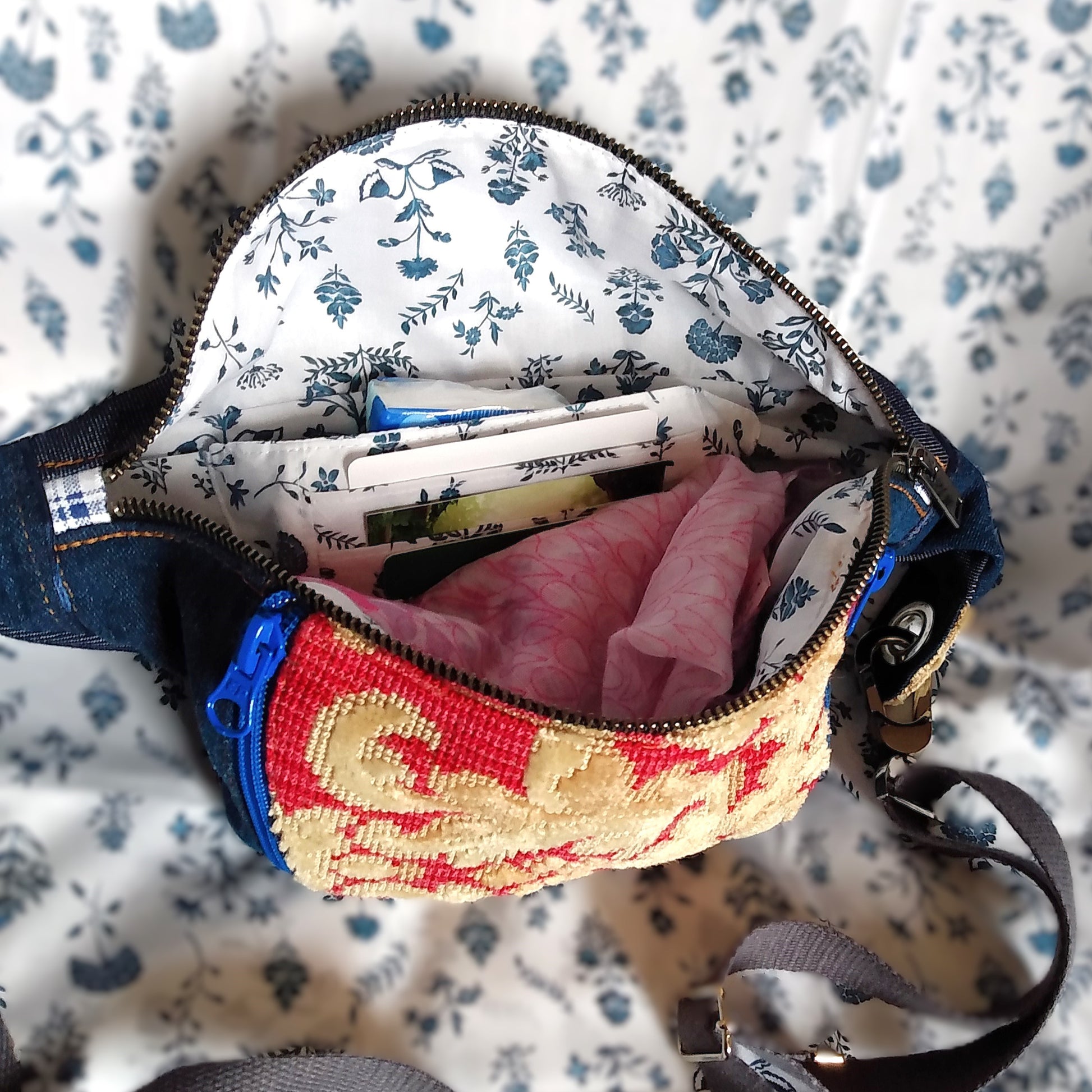 Vue intérieure du sac Mango. Le sac est ouvert via l'ouverture principale qui est une fermeture en métal. Il est rempli d'accessoires. On voit ainsi une poche avec 3 compartiments à cartes et une seconde poche à l'arrière. La doublure intérieure est blanche à fleurs bleues.