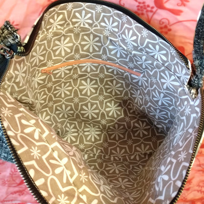 Intérieur du sac Laina. Le tissu de doublure est gris à motifs floraux blancs. Une poche zippée est présente sur l'arrière intérieur du sac. Elle se ferme avec un zip rose pâle.