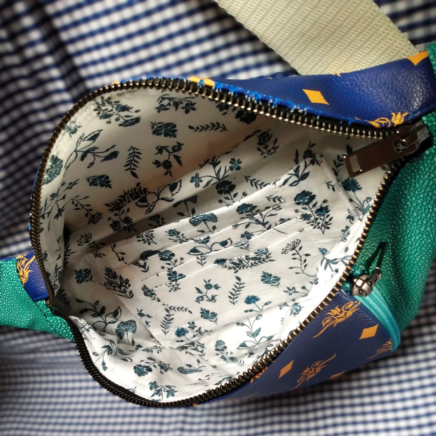 Vue intérieure de la banane version bleue. La poche principale s'ouvre via un zip métal. La doublure est blanche à fleurs bleues. On voit à l'intérieur de la banane , une poche et 3 compartiments à carte.